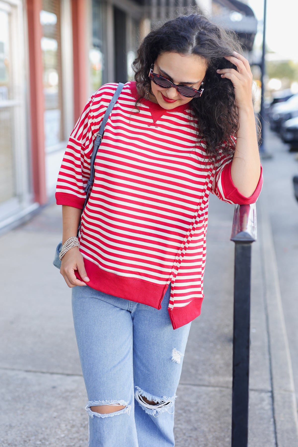 Woman wearing a red and white striped shirt and ripped jeans on a city street.