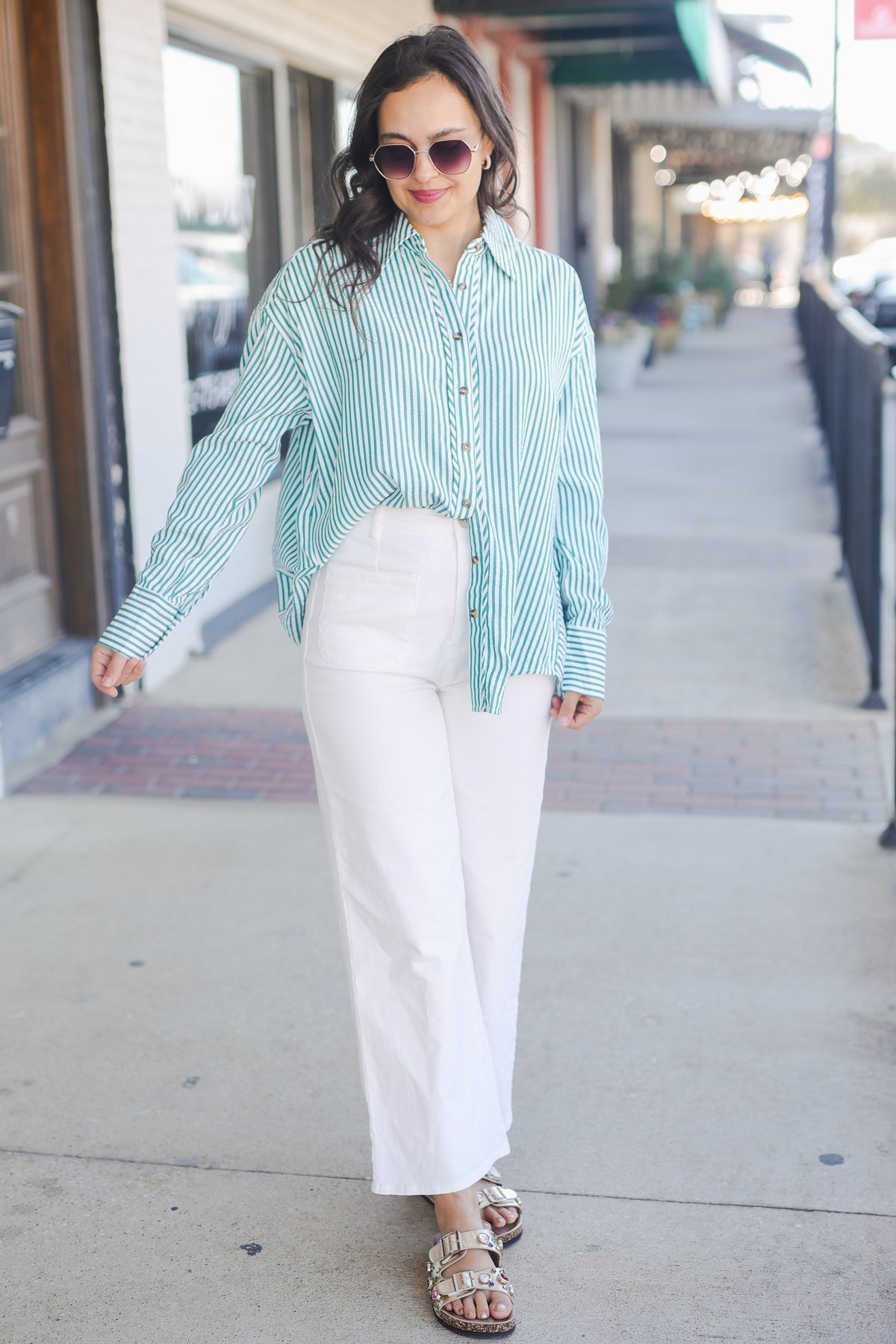 Woman wearing a green and white striped shirt and white pants on a sidewalk.