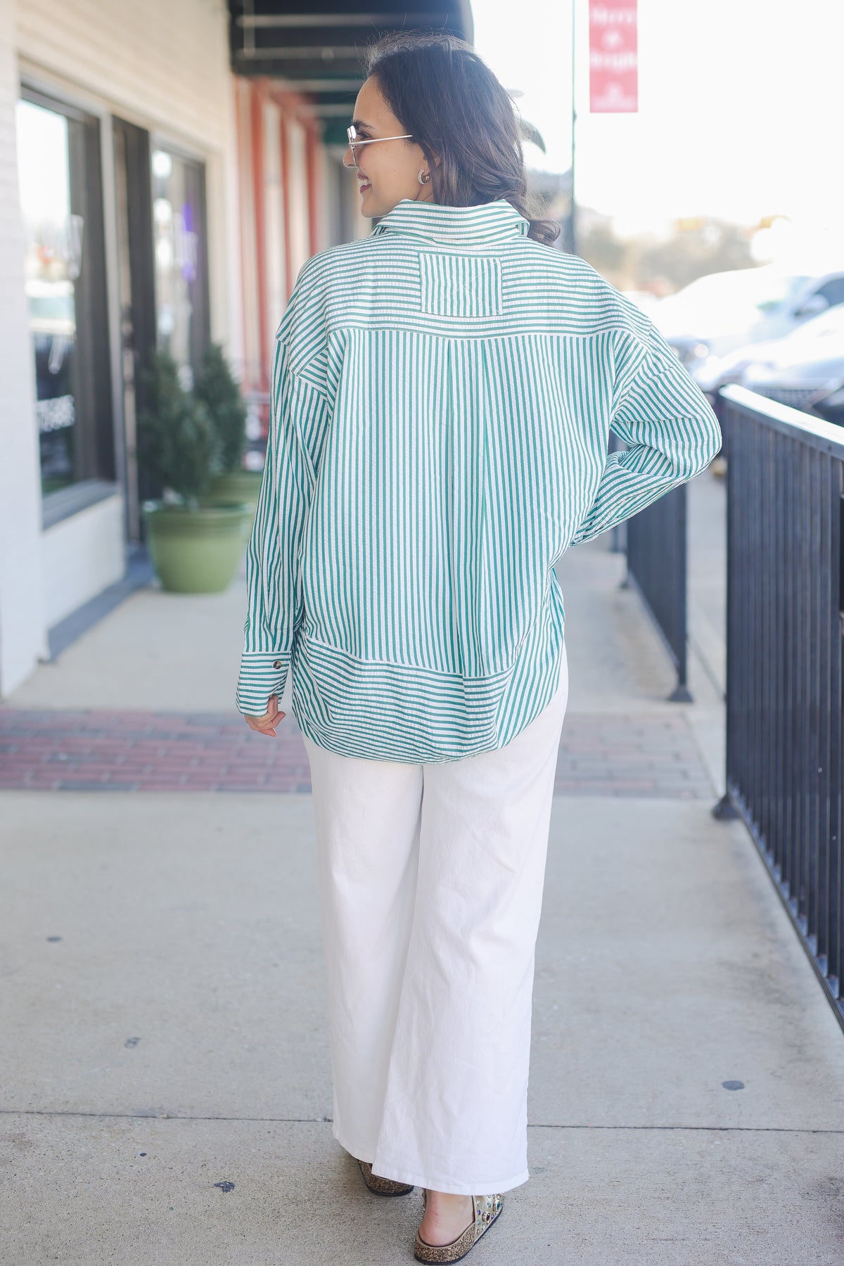 Woman wearing a green and white striped shirt and white pants on a sidewalk.