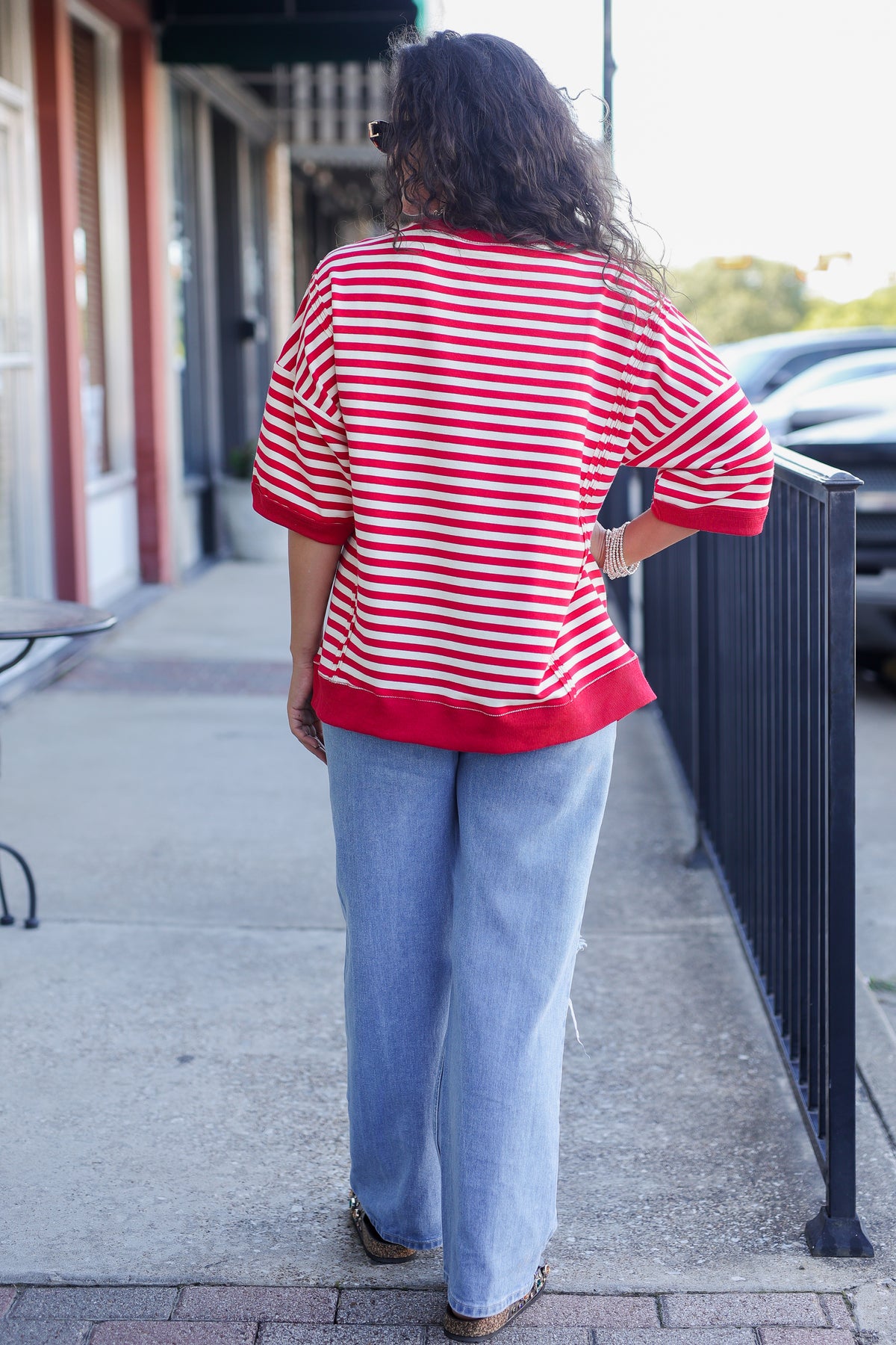 Person wearing a red and white striped shirt and blue jeans walking on a sidewalk.