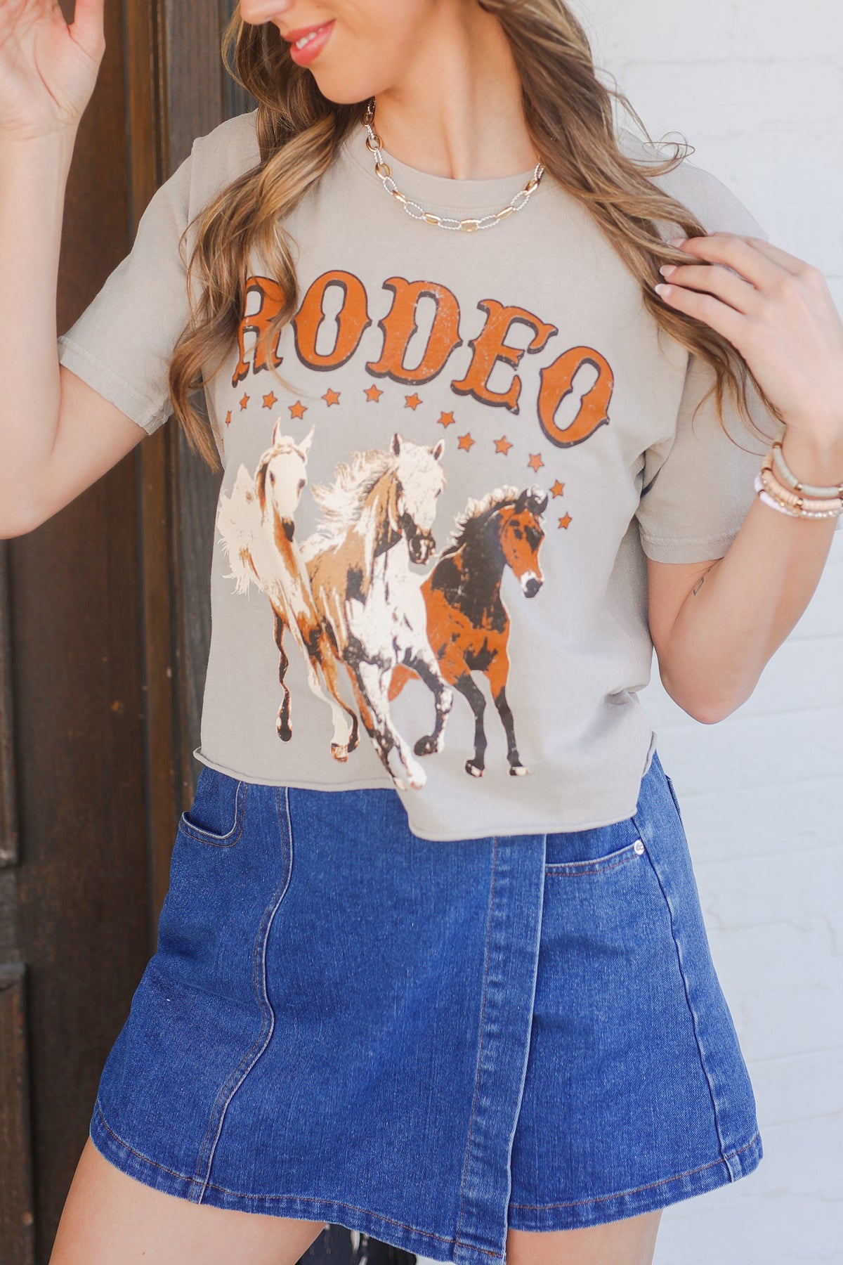 Woman wearing a 'Rodeo' graphic t-shirt with horses and a blue denim skirt.