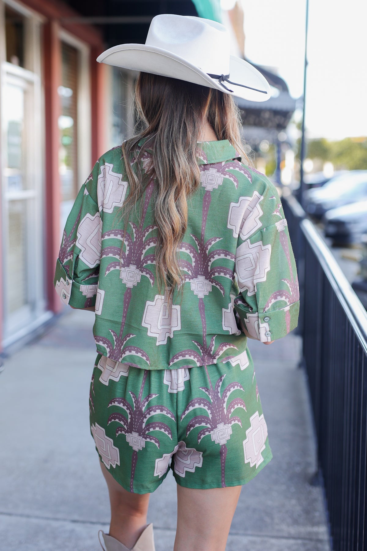 Person wearing a green patterned outfit with a cowboy hat on a city street.