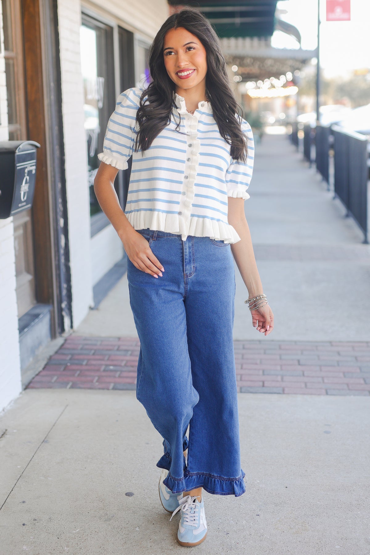 Woman wearing a striped shirt and blue jeans on a sidewalk.