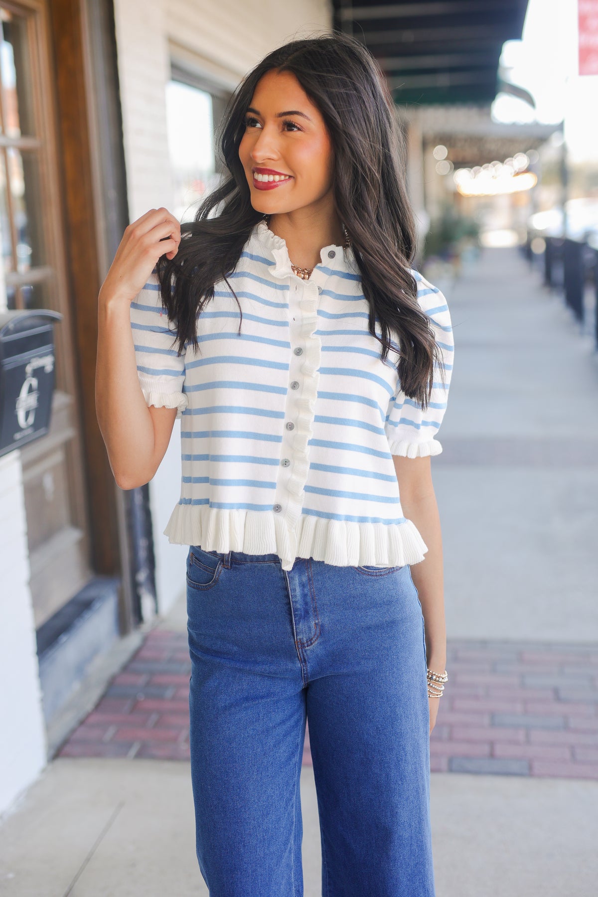Woman wearing a striped shirt and blue jeans on a city street.