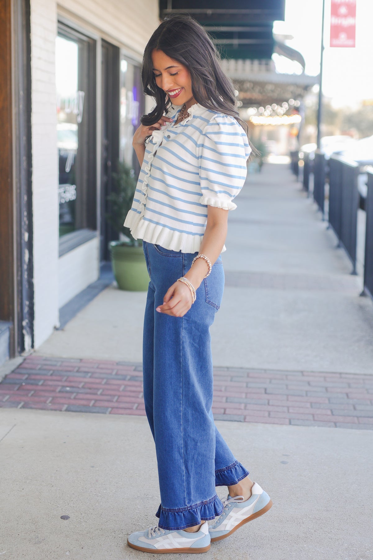 Woman wearing a striped shirt and blue jeans on a sidewalk.