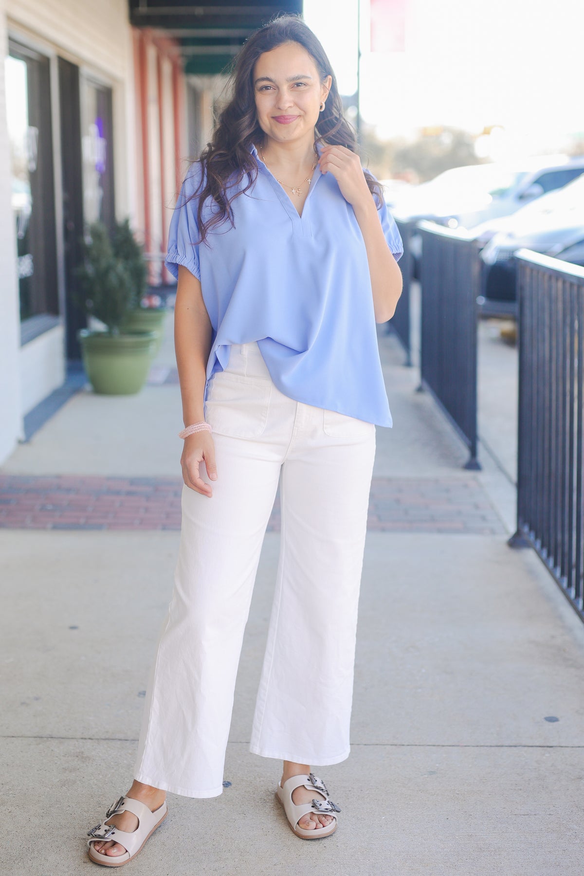 Woman wearing a light blue blouse and white pants on a sidewalk.