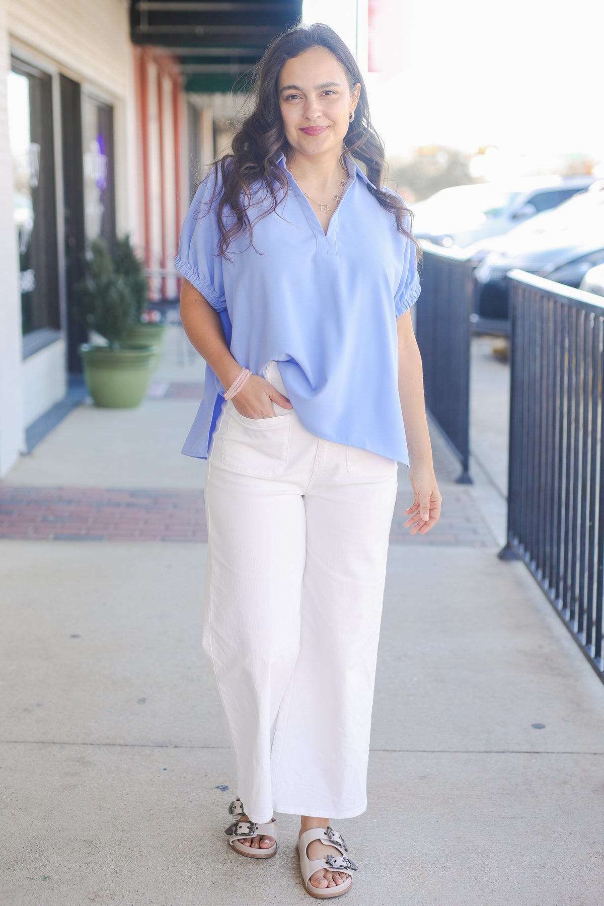 Woman wearing a light blue blouse and white pants on a sidewalk.