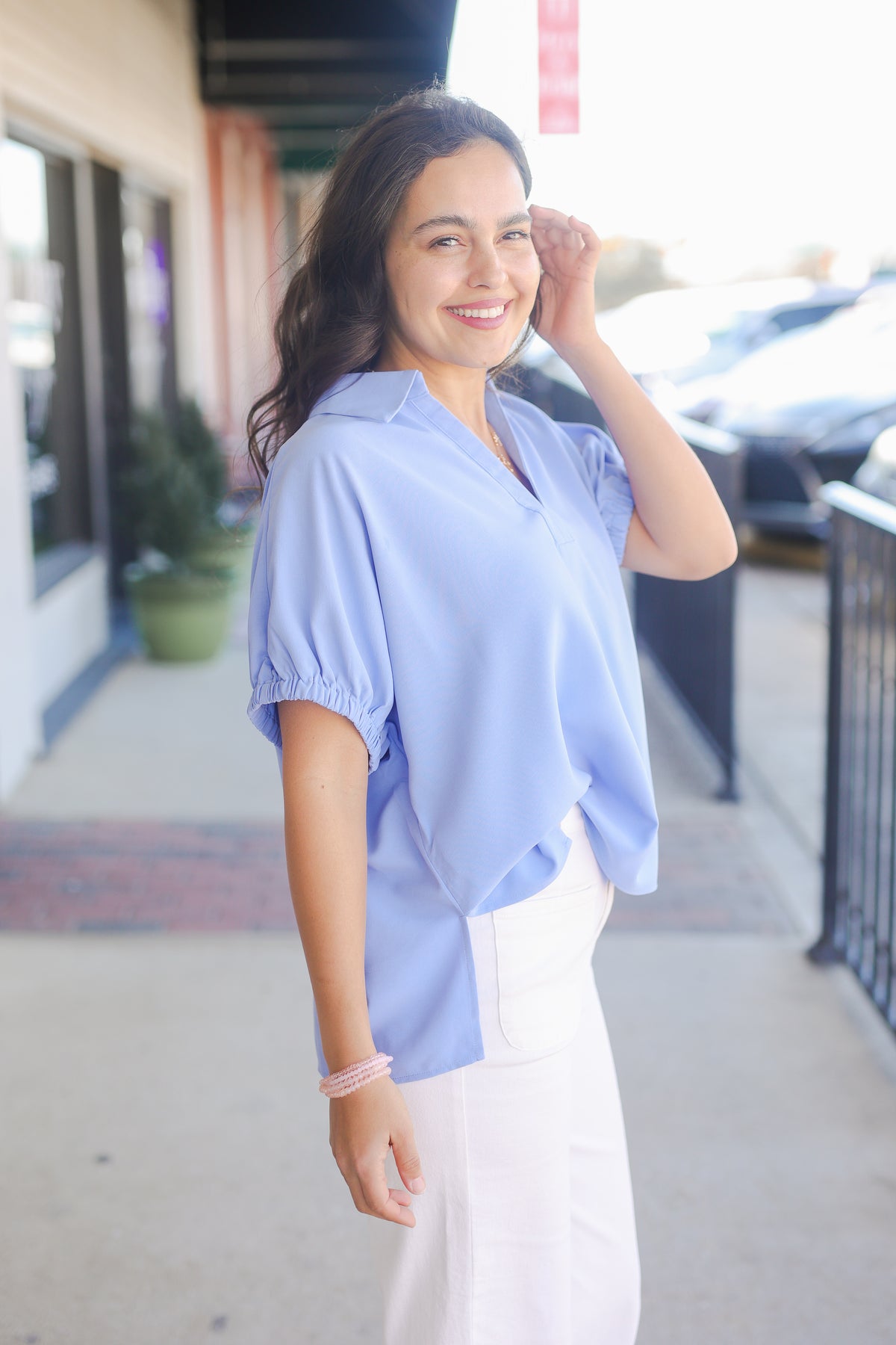 Woman wearing a light blue blouse and white pants standing on a sidewalk.