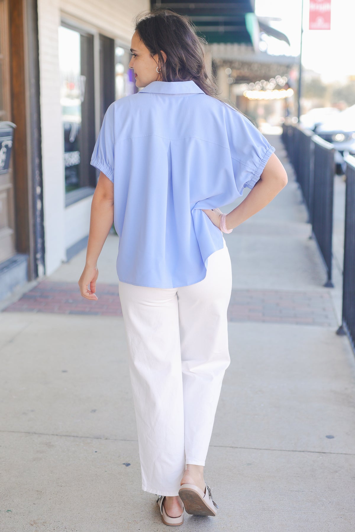 Woman wearing a light blue shirt and white pants walking on a sidewalk.