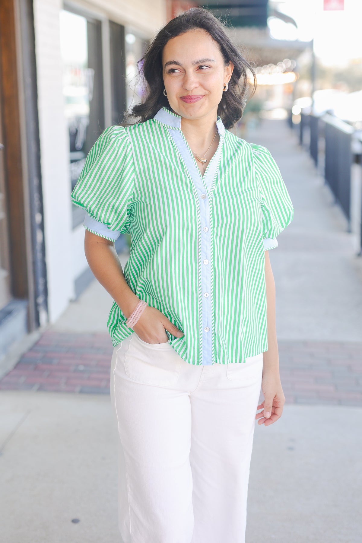 Woman wearing a green and white striped shirt with white pants on a city street.