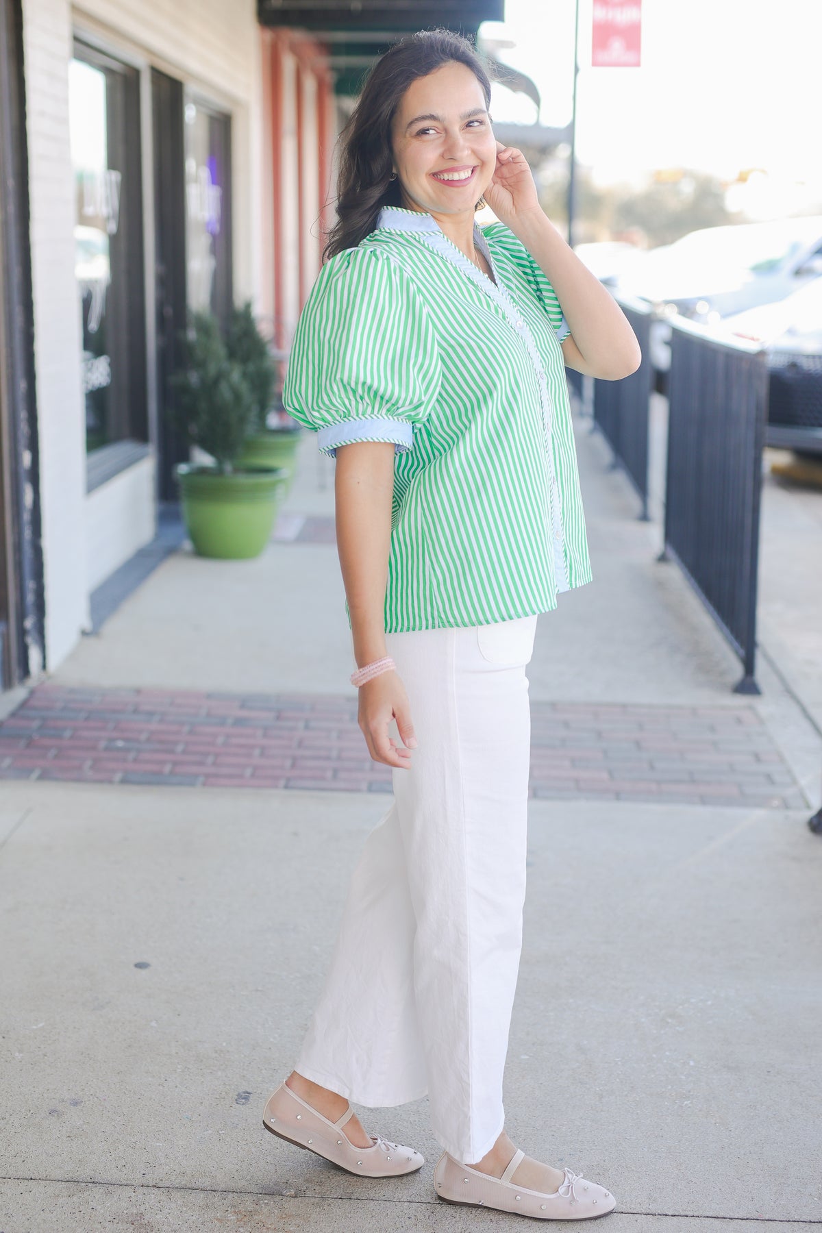 Woman wearing a green and white striped shirt and white pants on a sidewalk.