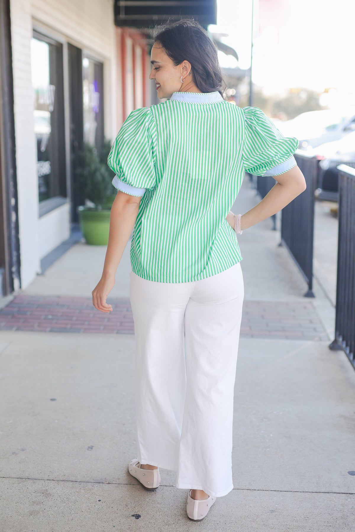 Woman wearing a green and white striped shirt and white pants on a sidewalk.