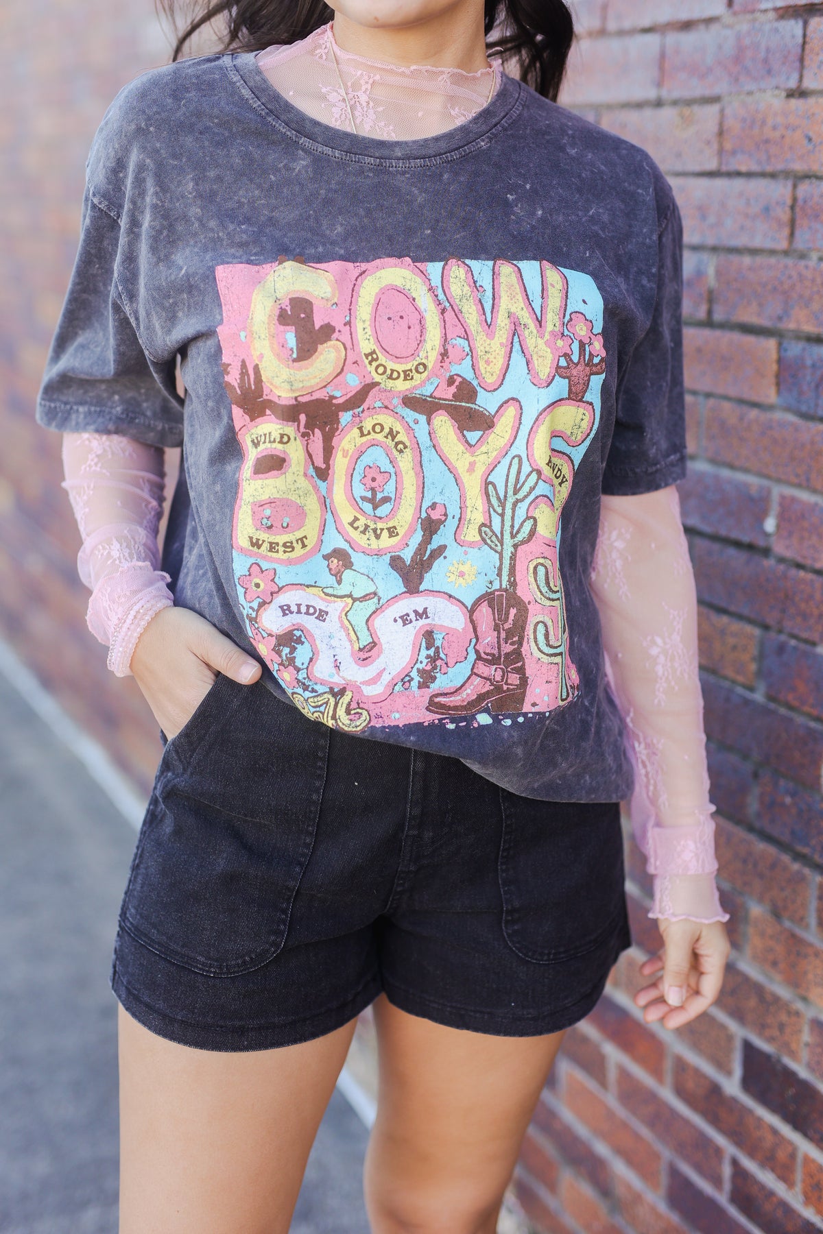 Person wearing a graphic t-shirt with colorful text and graphics against a brick wall.