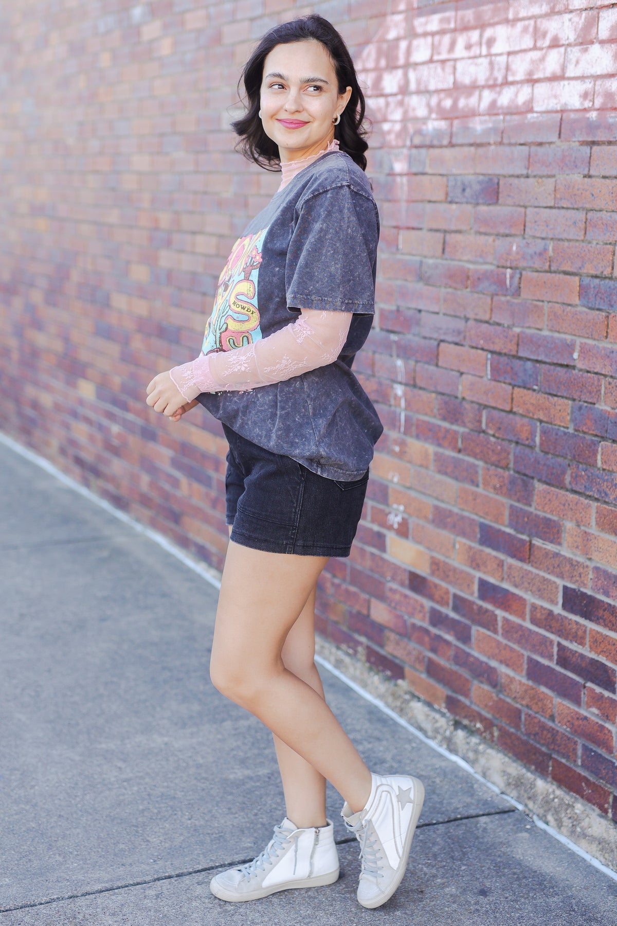 Woman standing against a brick wall wearing a graphic t-shirt and shorts.