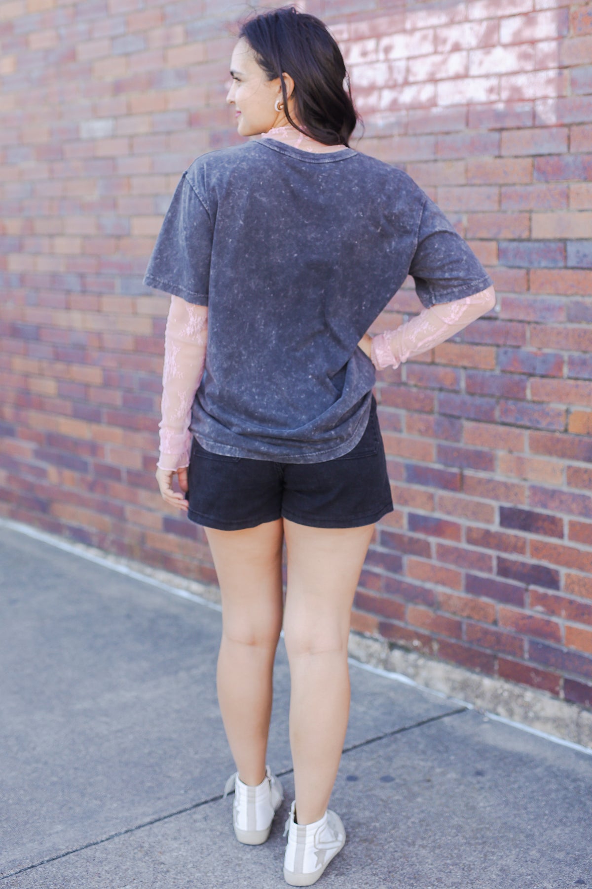 Person wearing a gray t-shirt and black shorts standing against a brick wall.