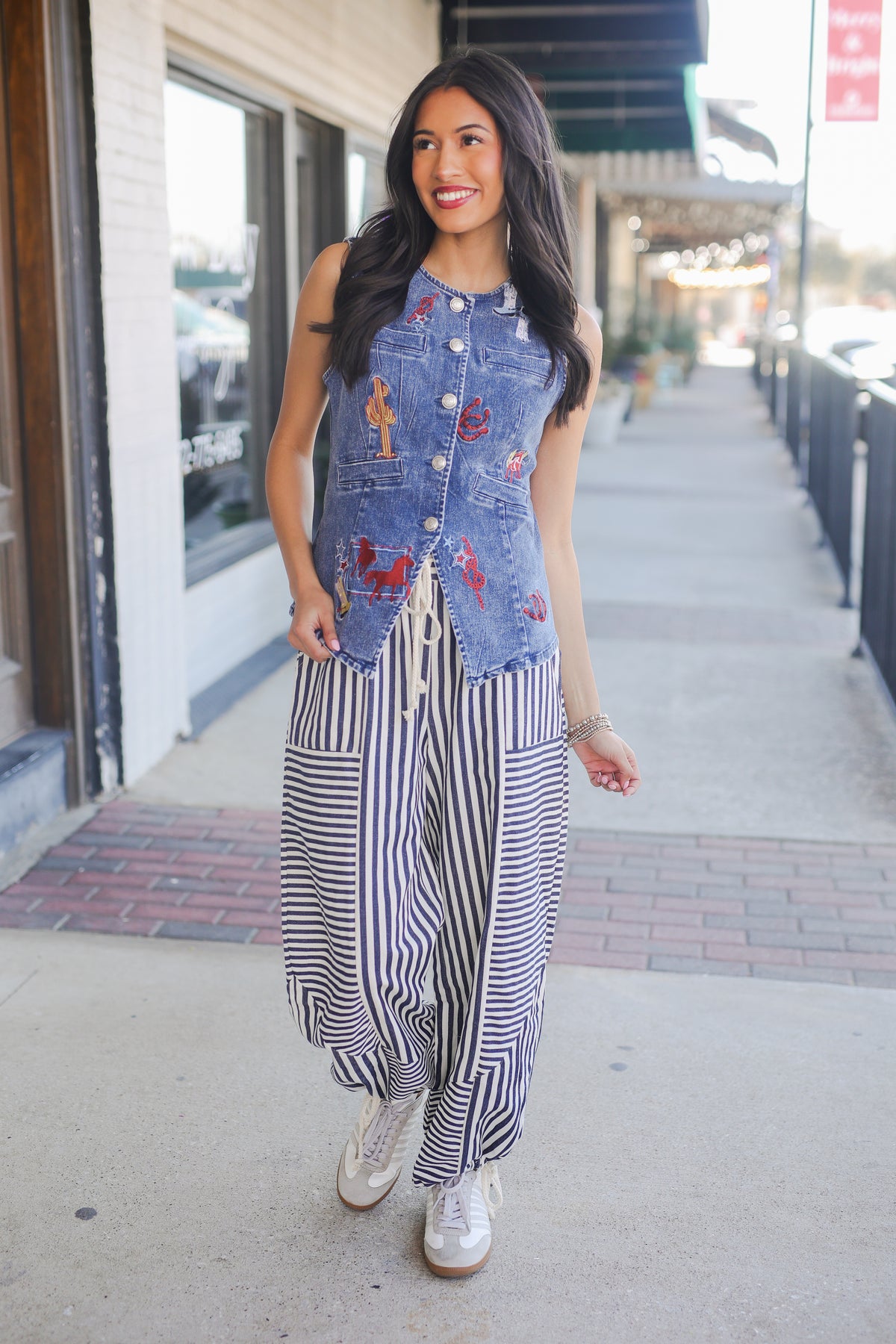 Woman wearing a denim vest over a striped outfit on a city street.