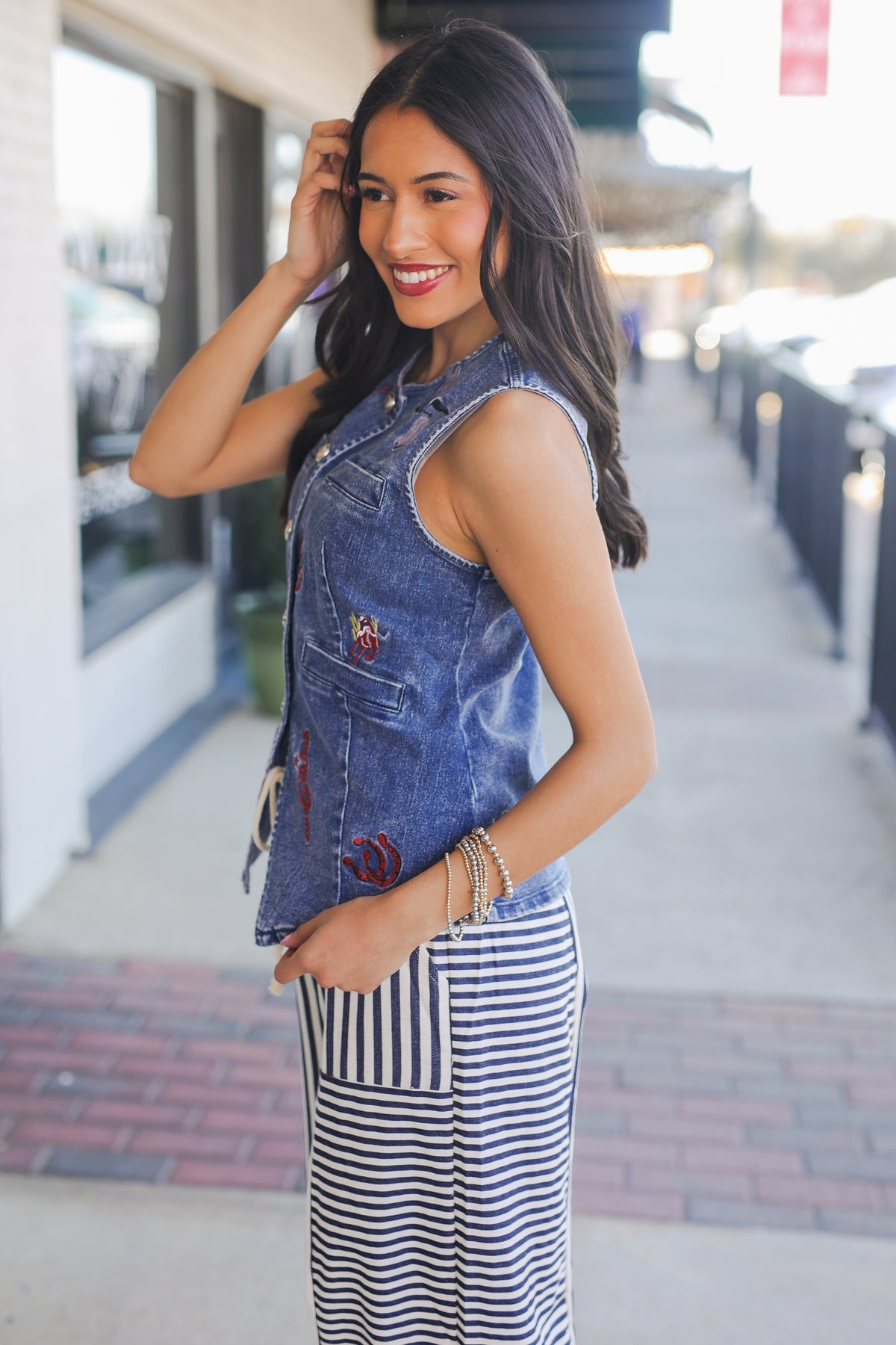 Woman wearing a denim vest and striped pants on a city street.