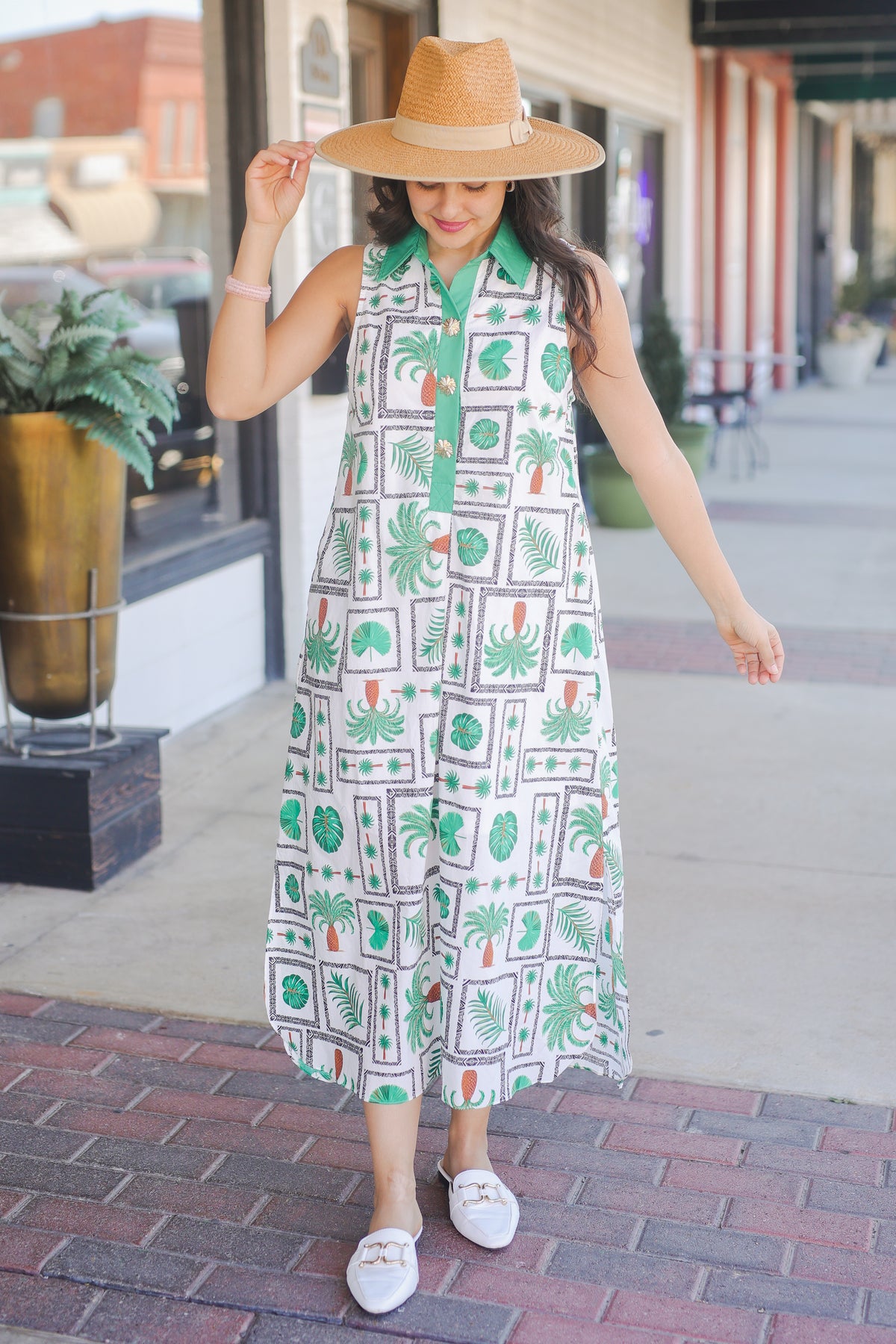 Woman wearing a patterned dress and straw hat on a city street.