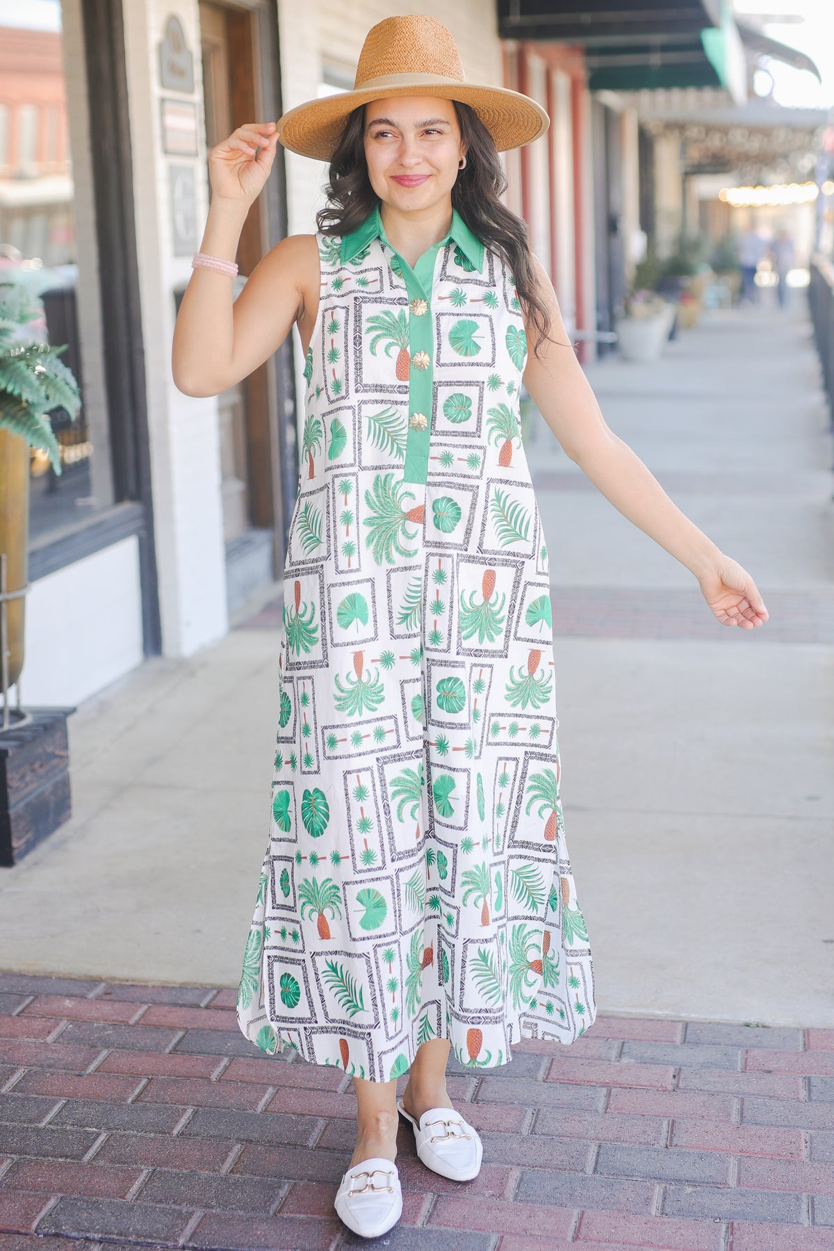 Woman wearing a sleeveless dress with a pattern, standing on a sidewalk.