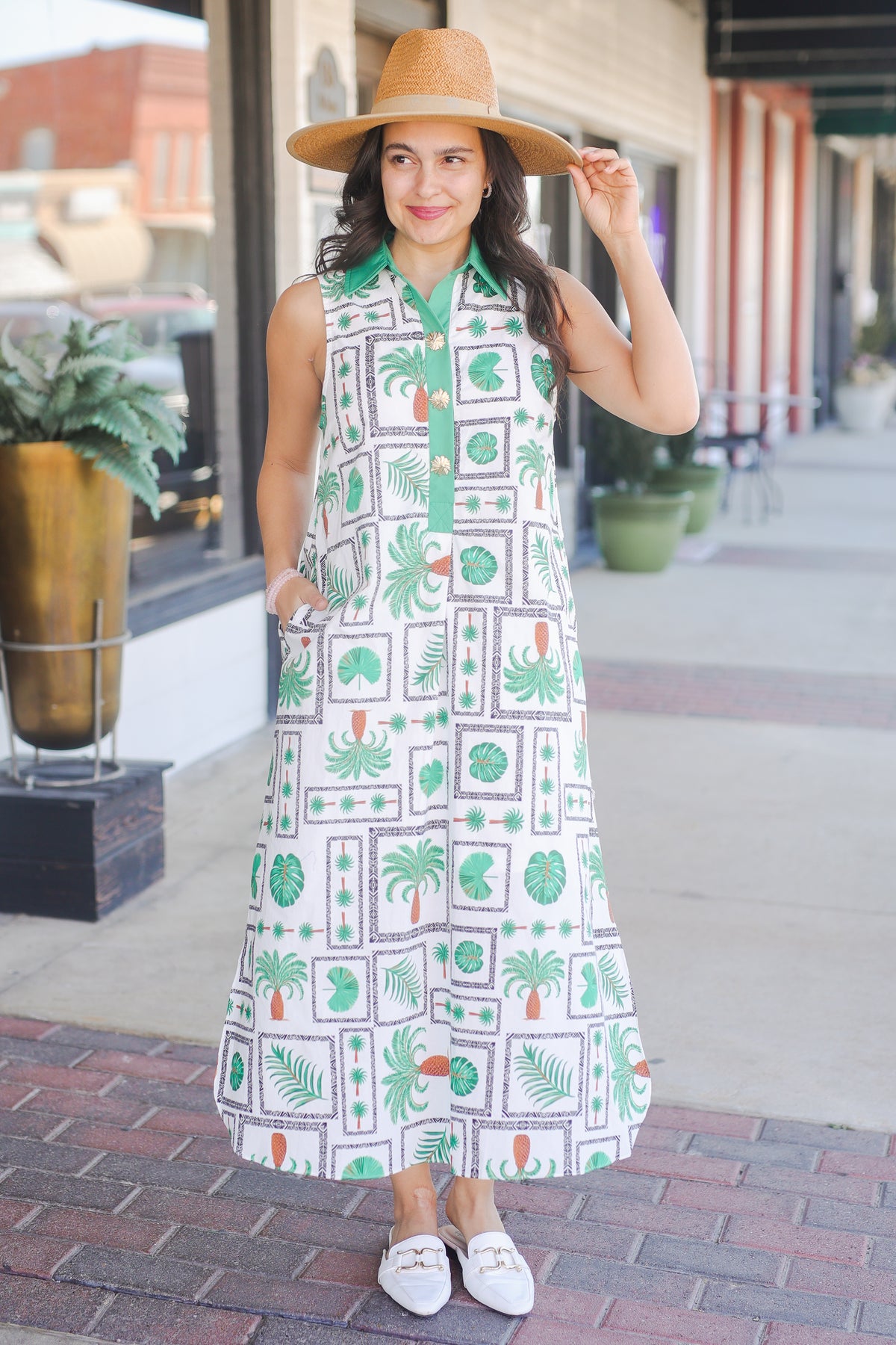 Woman wearing a patterned dress and hat on a city street.