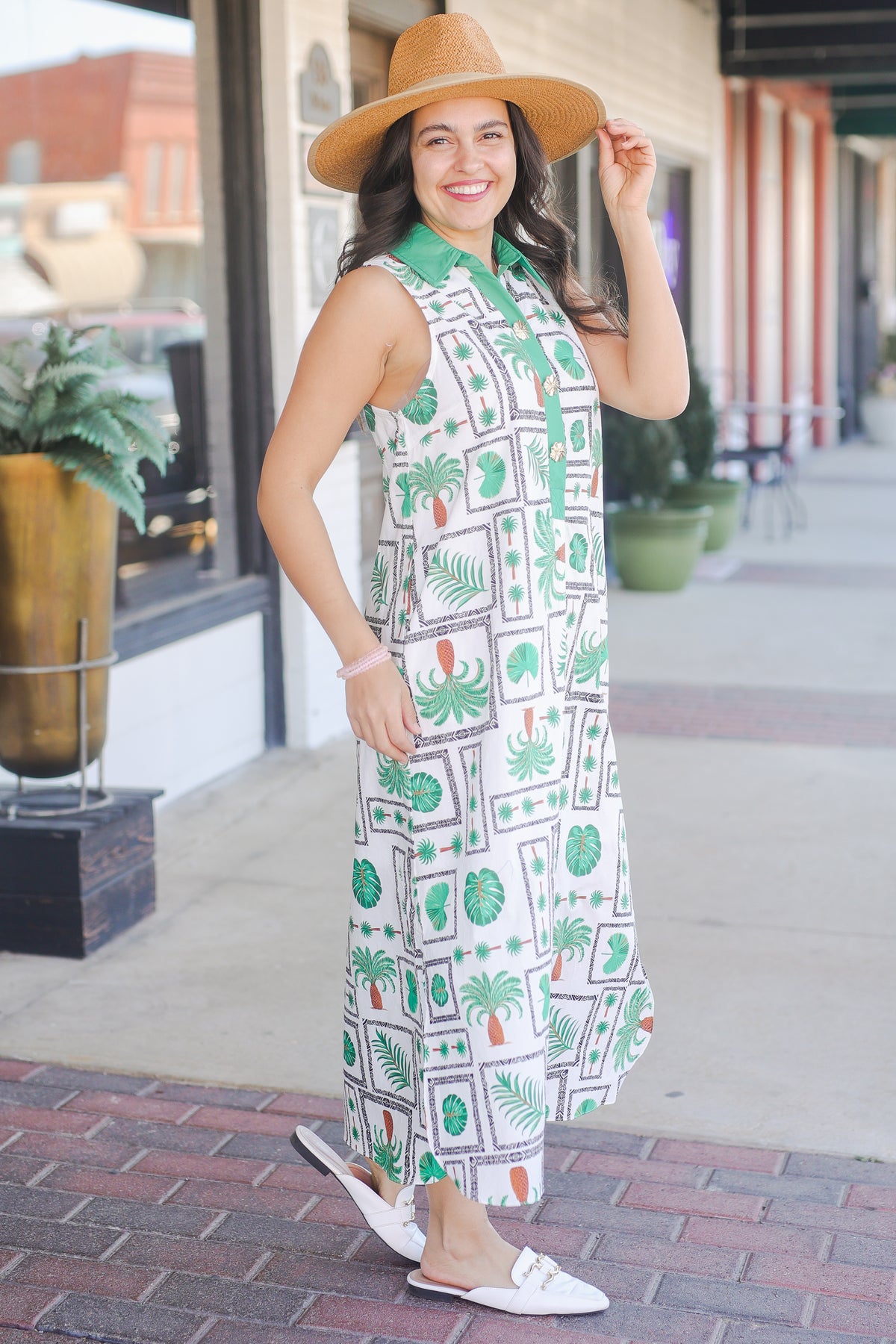 Woman wearing a patterned dress and hat on a city street.