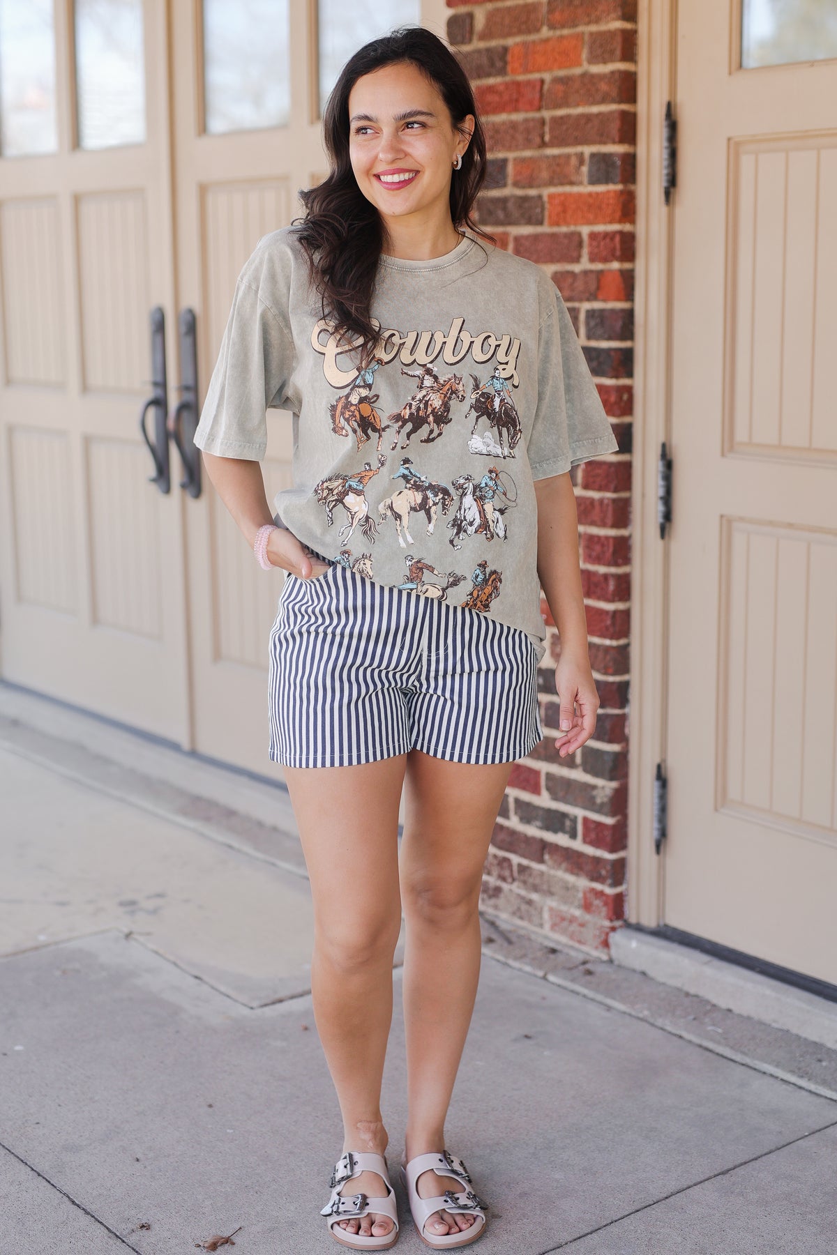 Woman wearing a graphic t-shirt and striped shorts standing in front of a brick wall.