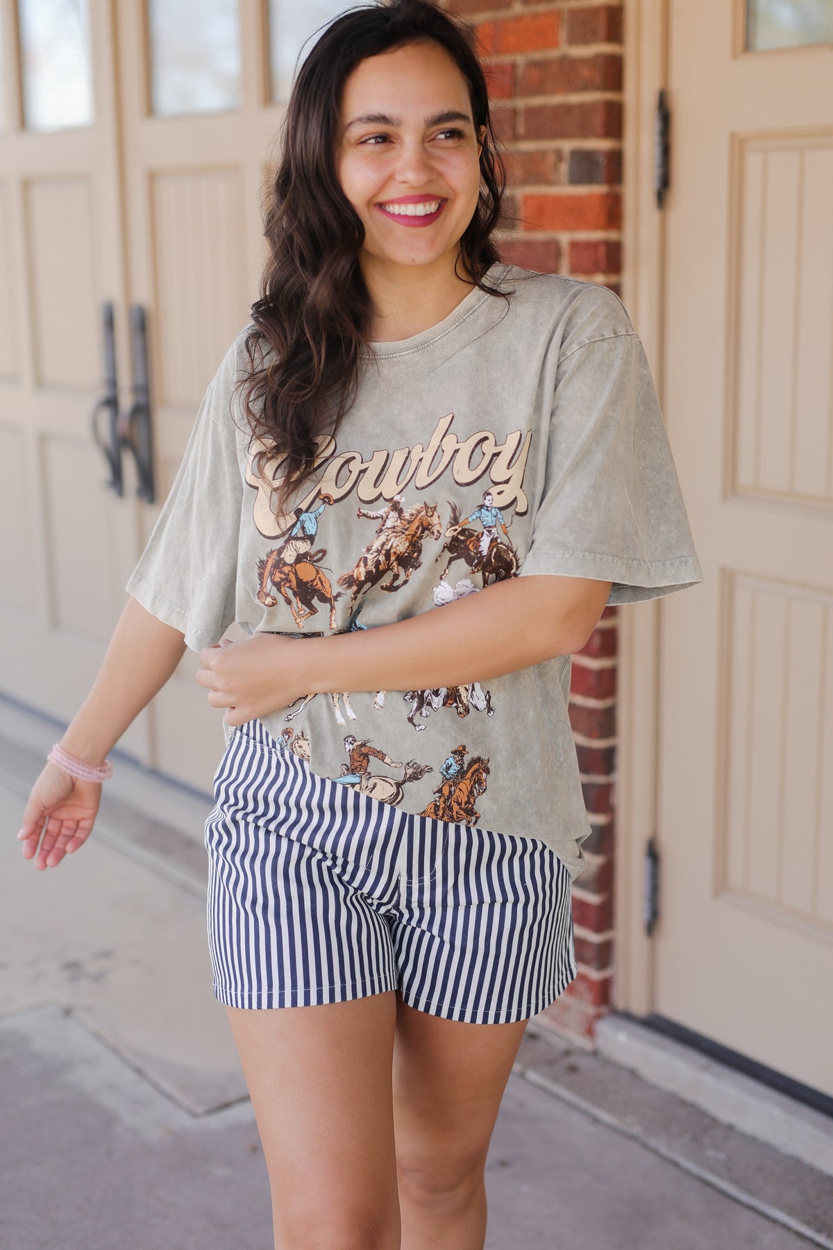 Woman wearing a graphic t-shirt with 'Cowboy' text and horse images, standing in front of a door.