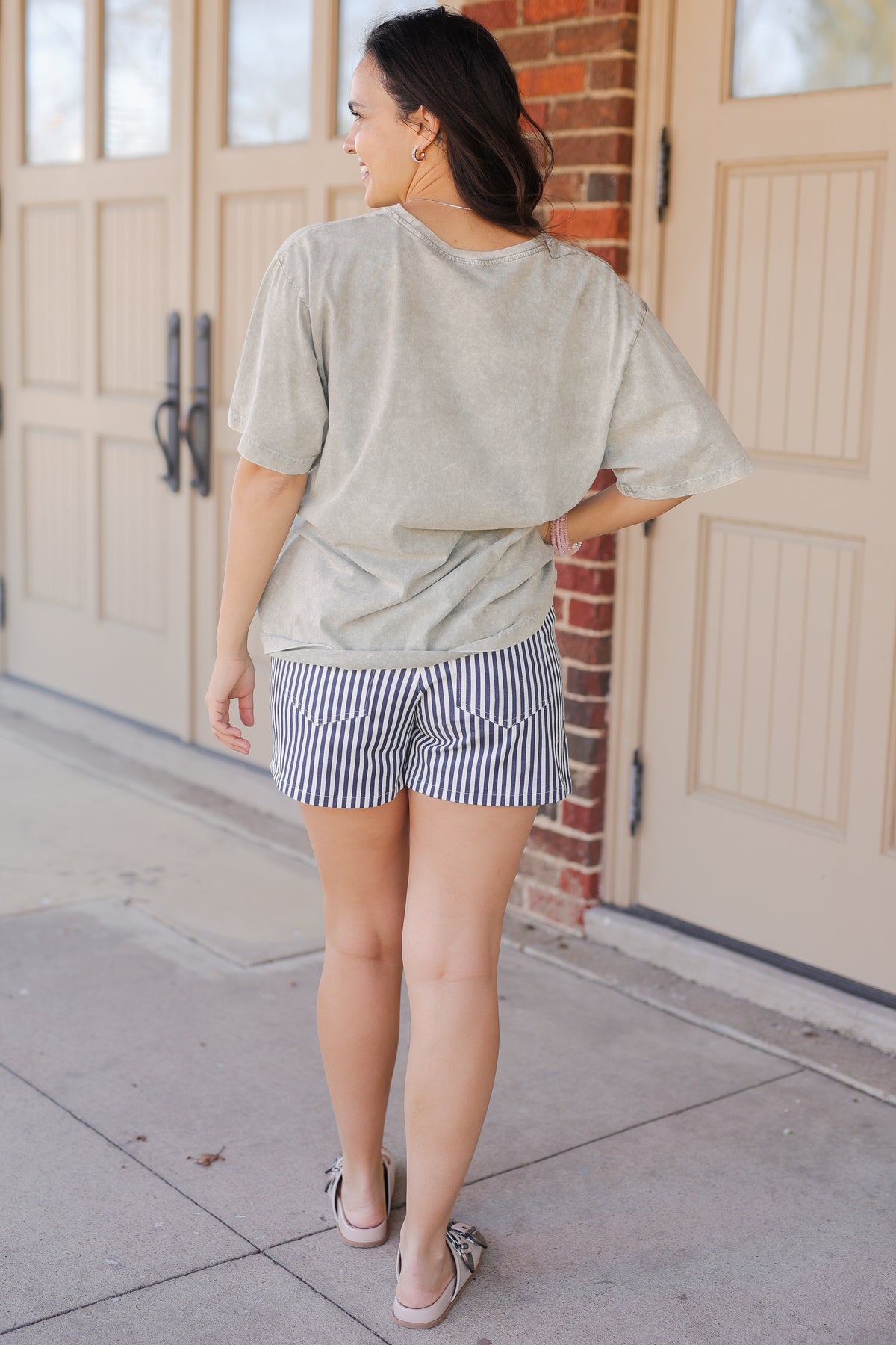 Woman wearing a light gray t-shirt and striped shorts standing in front of a garage door.