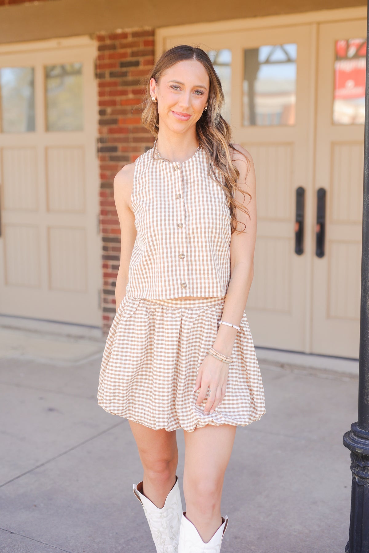 Woman wearing a checkered tank and skirt and white boots standing in front of a building.