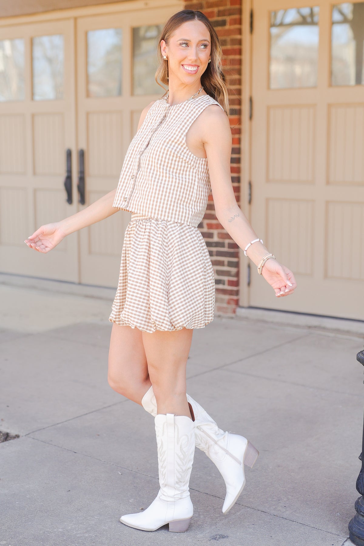 Woman wearing a checkered tank and skirt and white boots standing in front of a building.