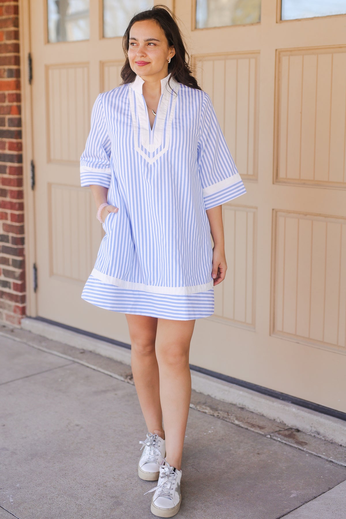 Woman wearing a blue and white striped dress with sneakers standing in front of a garage door.