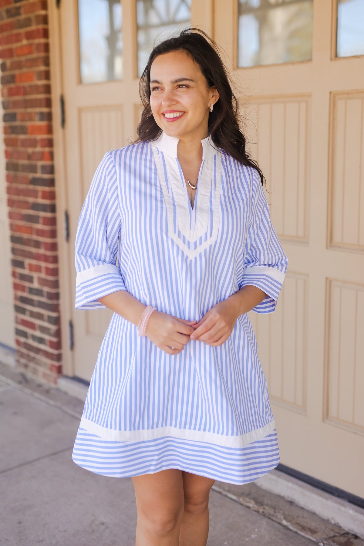 Woman wearing a blue and white striped dress with a white scarf in front of a beige door.