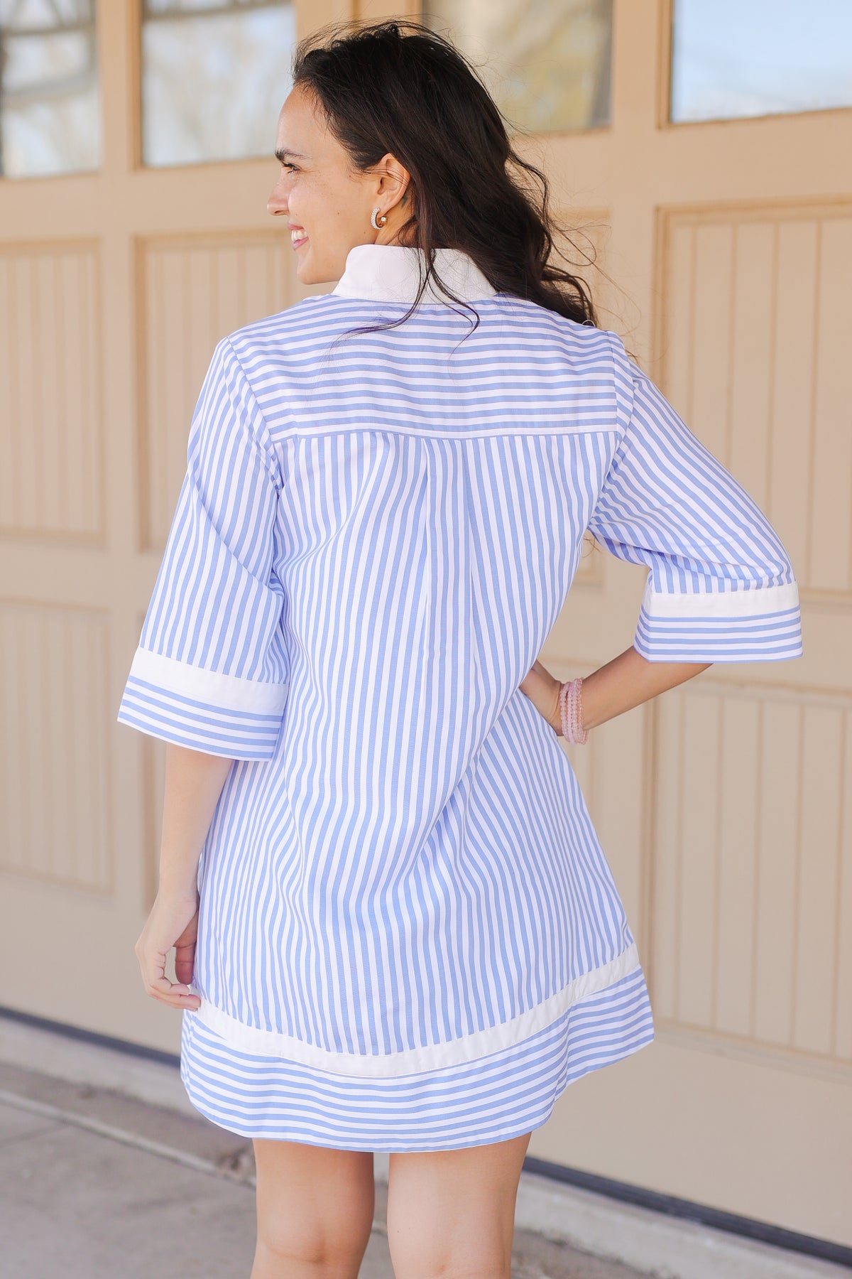 Woman wearing a blue and white striped dress standing in front of a wooden door.