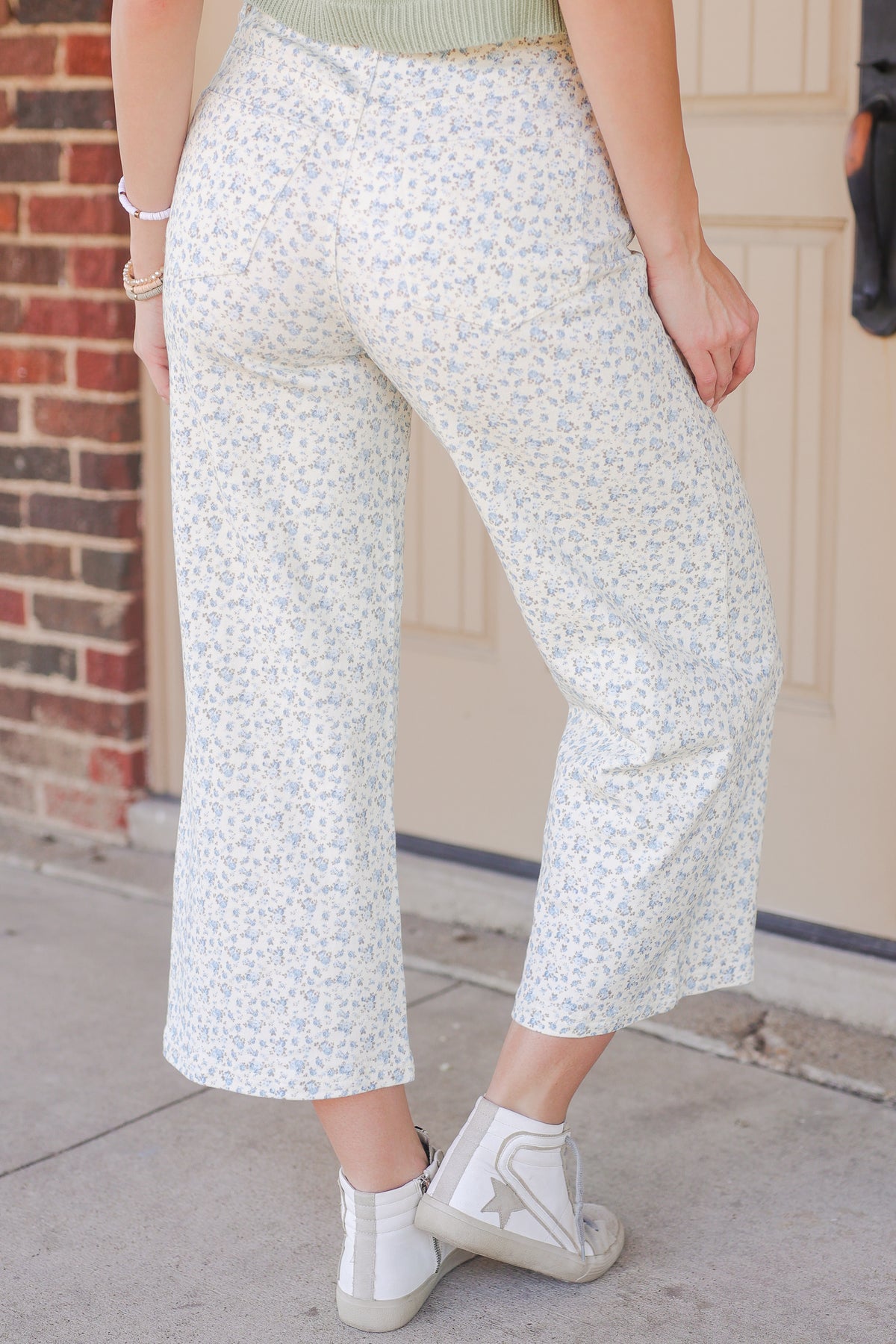 Person wearing white floral pants standing in front of a beige wall.