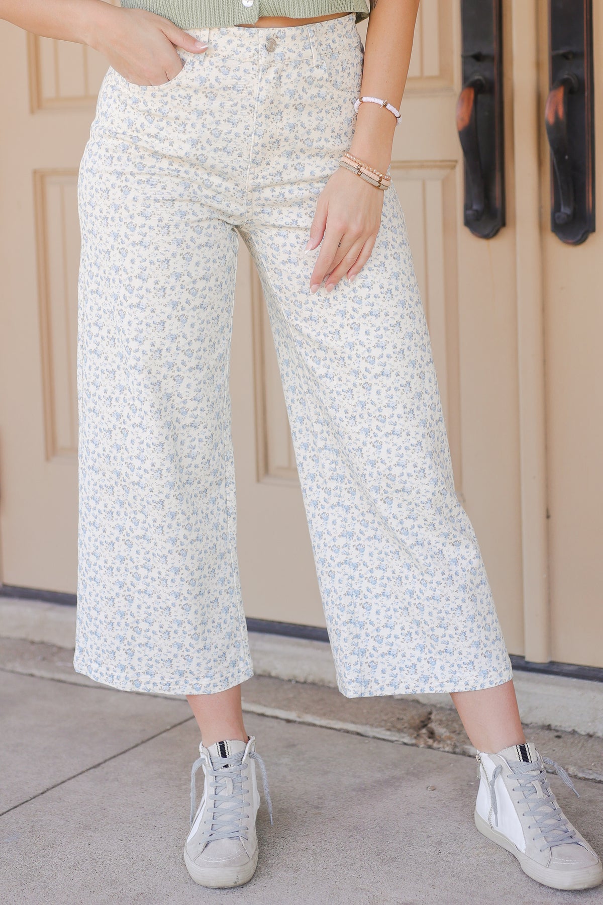 Person wearing white patterned pants and white sneakers in front of a beige wall.