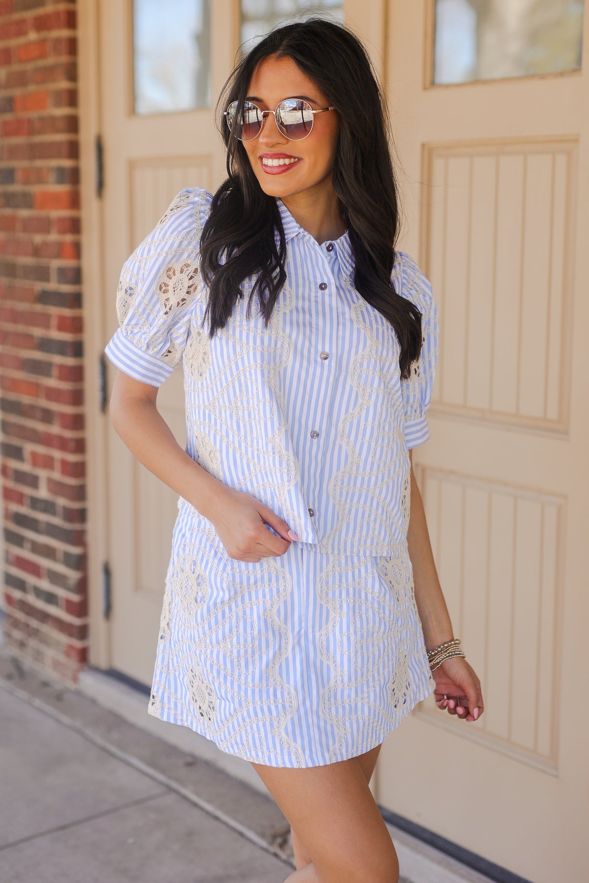 Woman wearing a blue and white striped dress with embroidery, standing in front of a door.