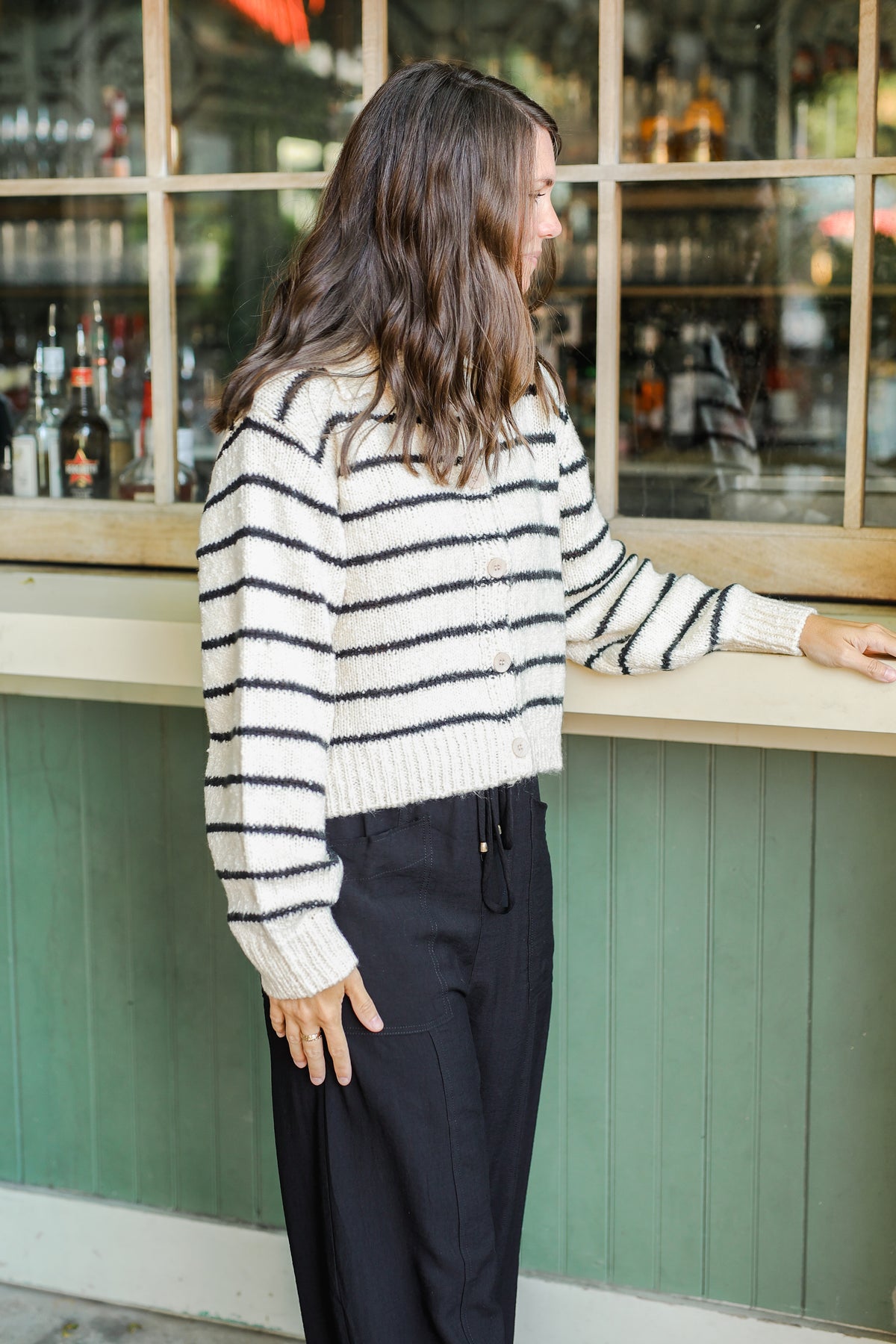 Person wearing a striped sweater and dark pants standing in front of a bar.