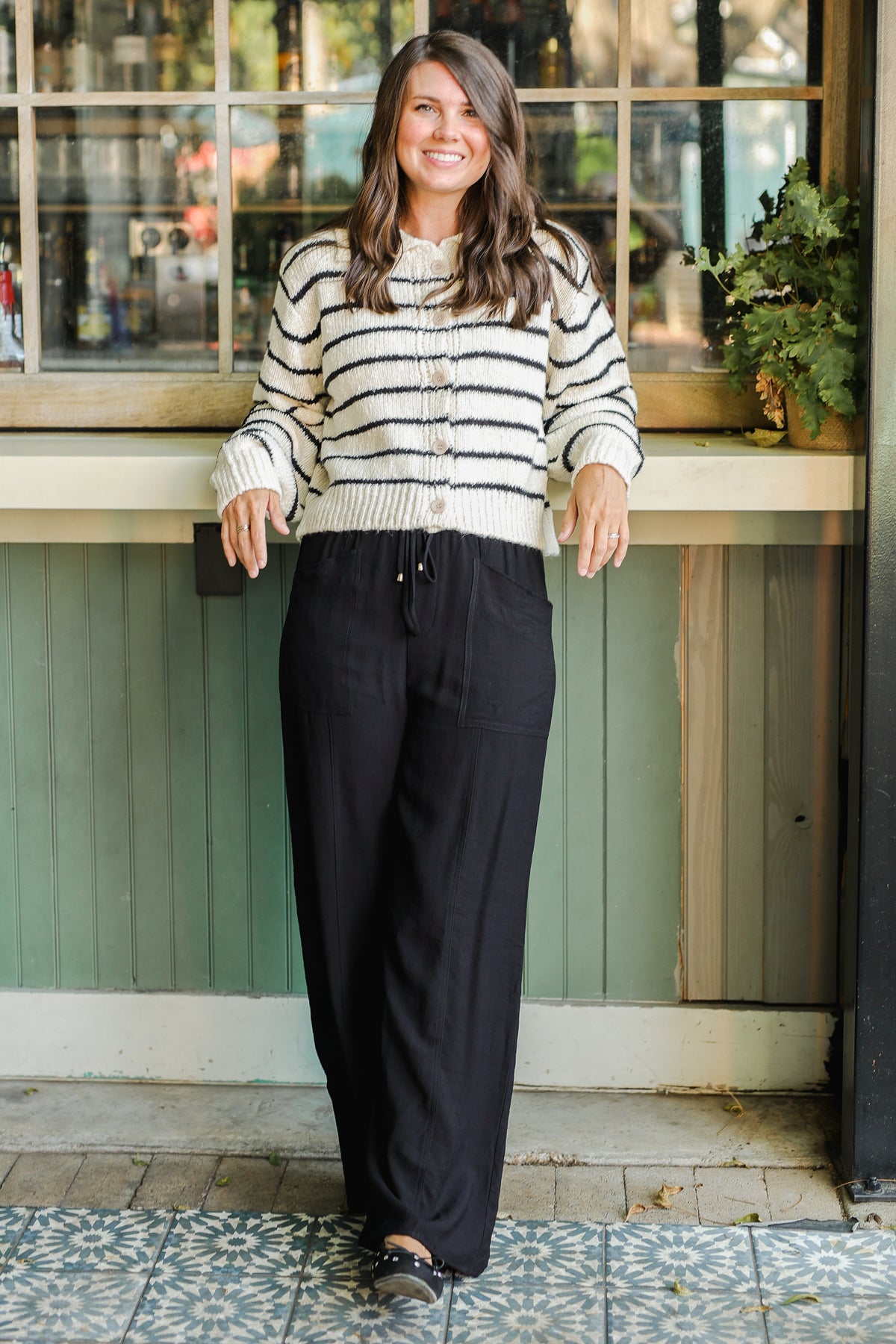 Woman wearing a striped sweater and black pants standing outside a building.