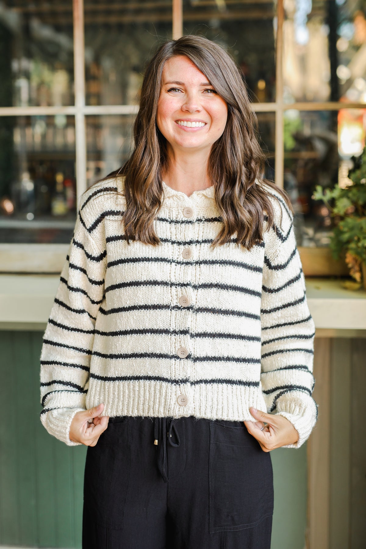 Woman wearing a striped sweater standing in front of a store window.