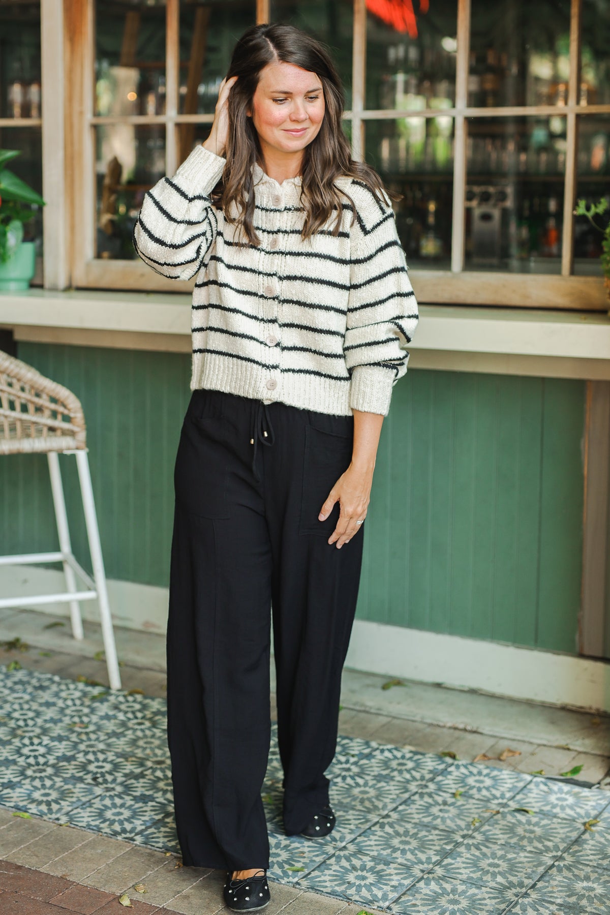 Woman wearing a striped sweater and black pants standing outdoors.