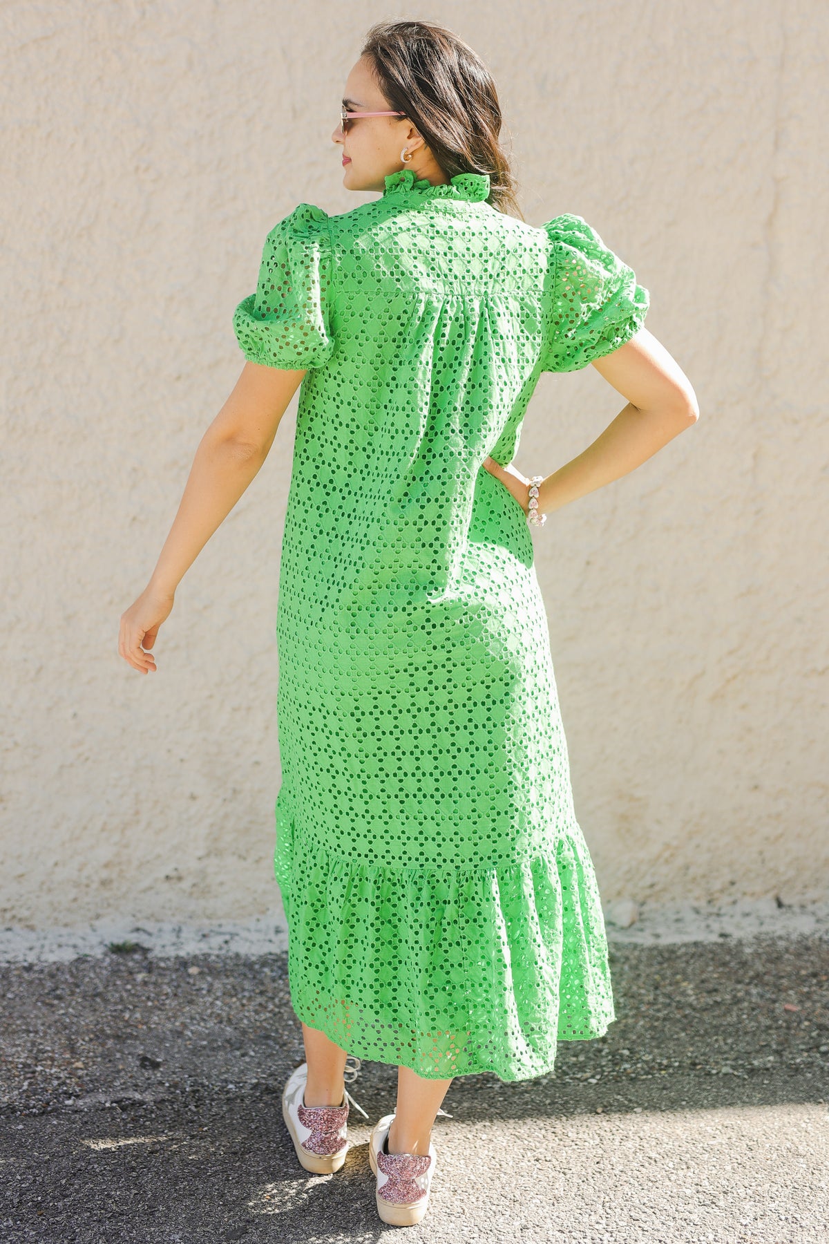 Woman wearing a green dress with a white pattern against a plain wall.