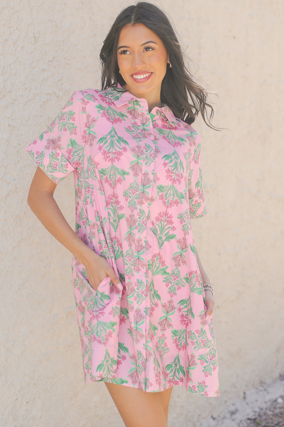 Woman wearing a pink floral dress against a beige wall