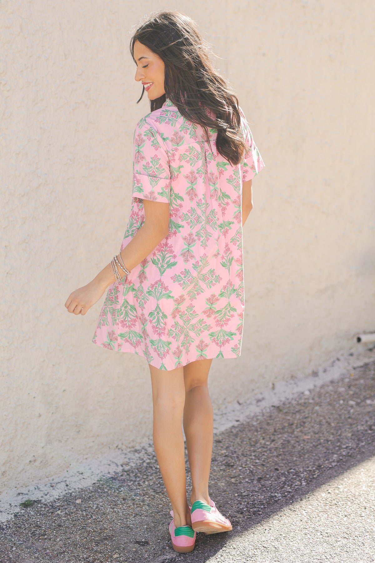 Woman wearing a pink floral dress against a beige wall.