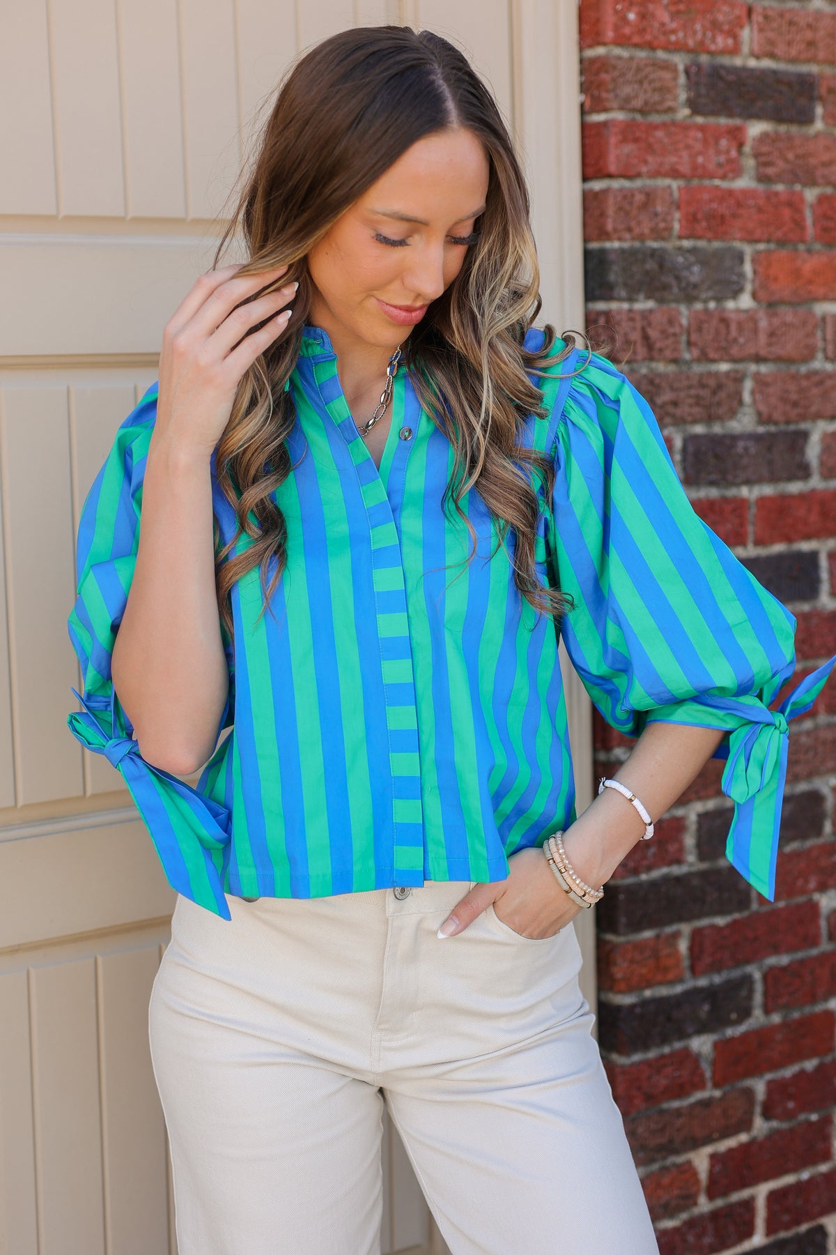 Woman wearing a blue and green striped blouse with tied sleeves against a brick wall.