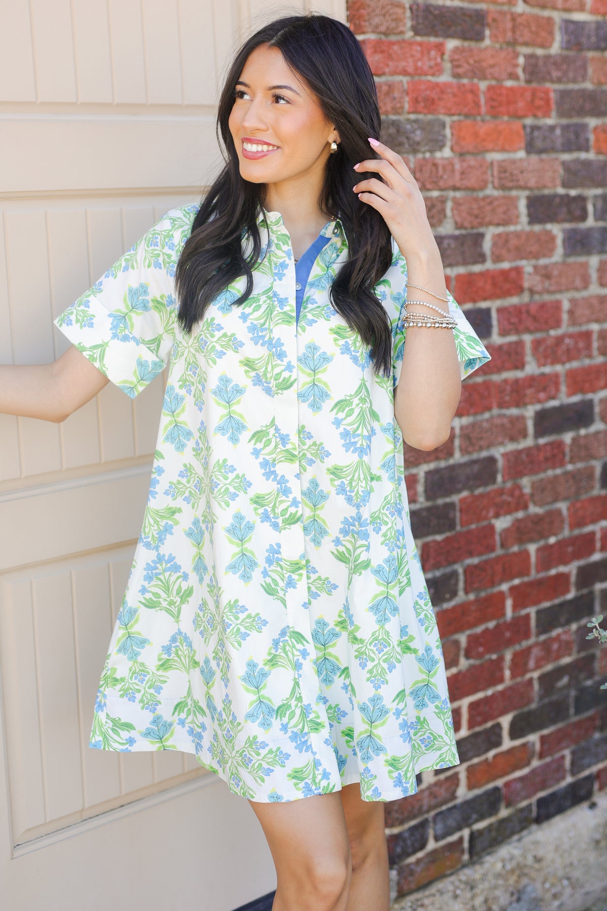 Woman wearing a floral dress standing in front of a brick wall.