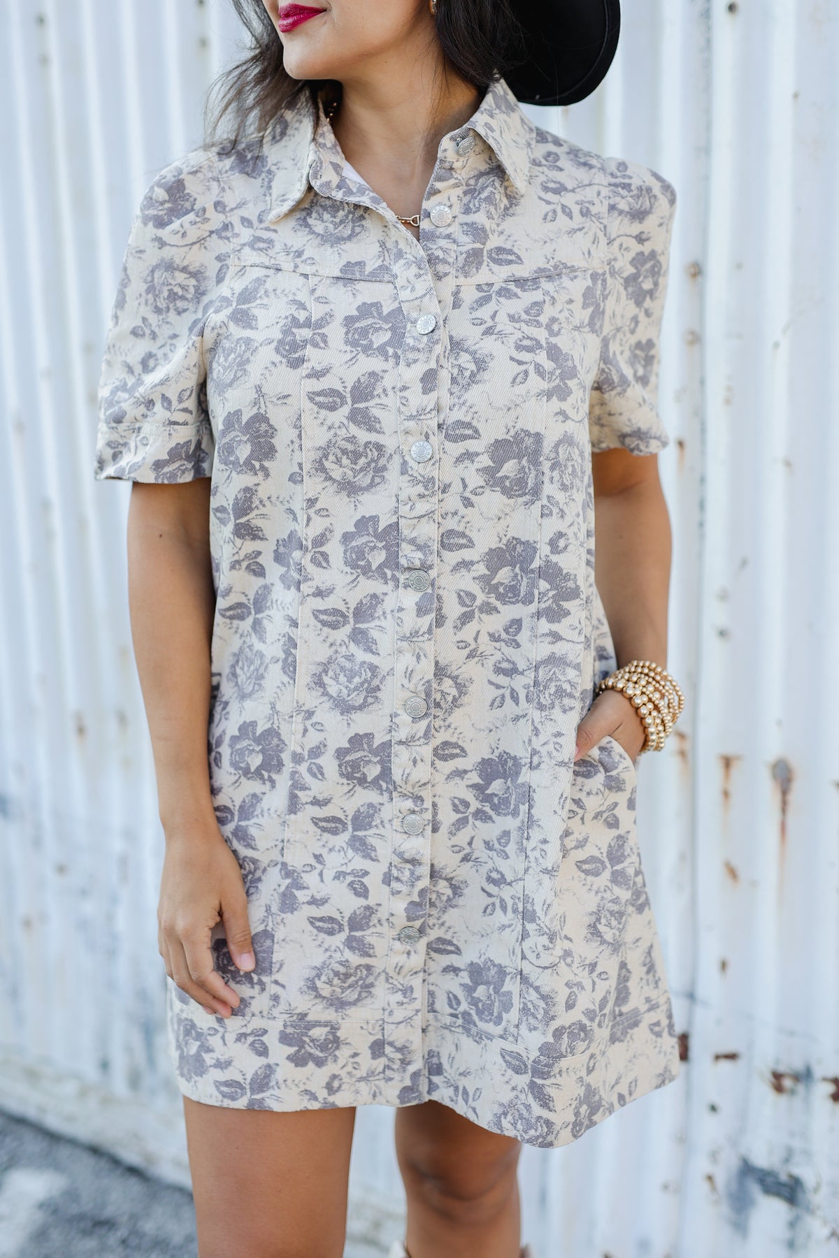 Woman wearing a floral dress against a white wall.