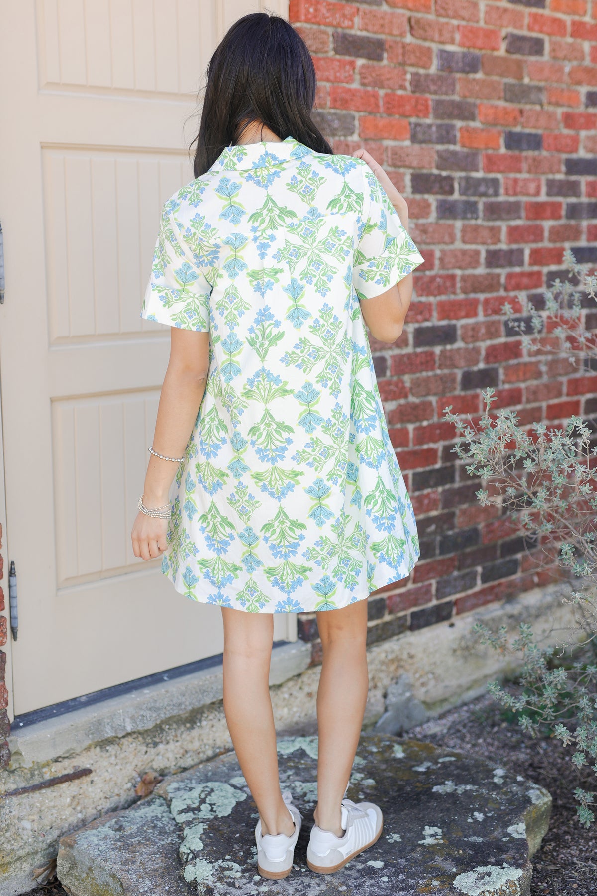 Person wearing a floral dress standing in front of a brick wall.