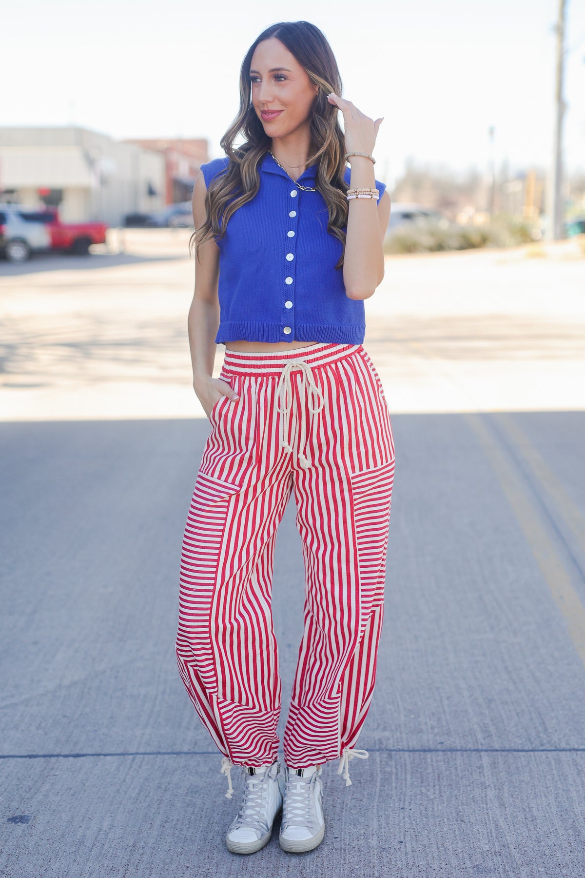 Woman wearing a blue top and red striped pants standing on a street.