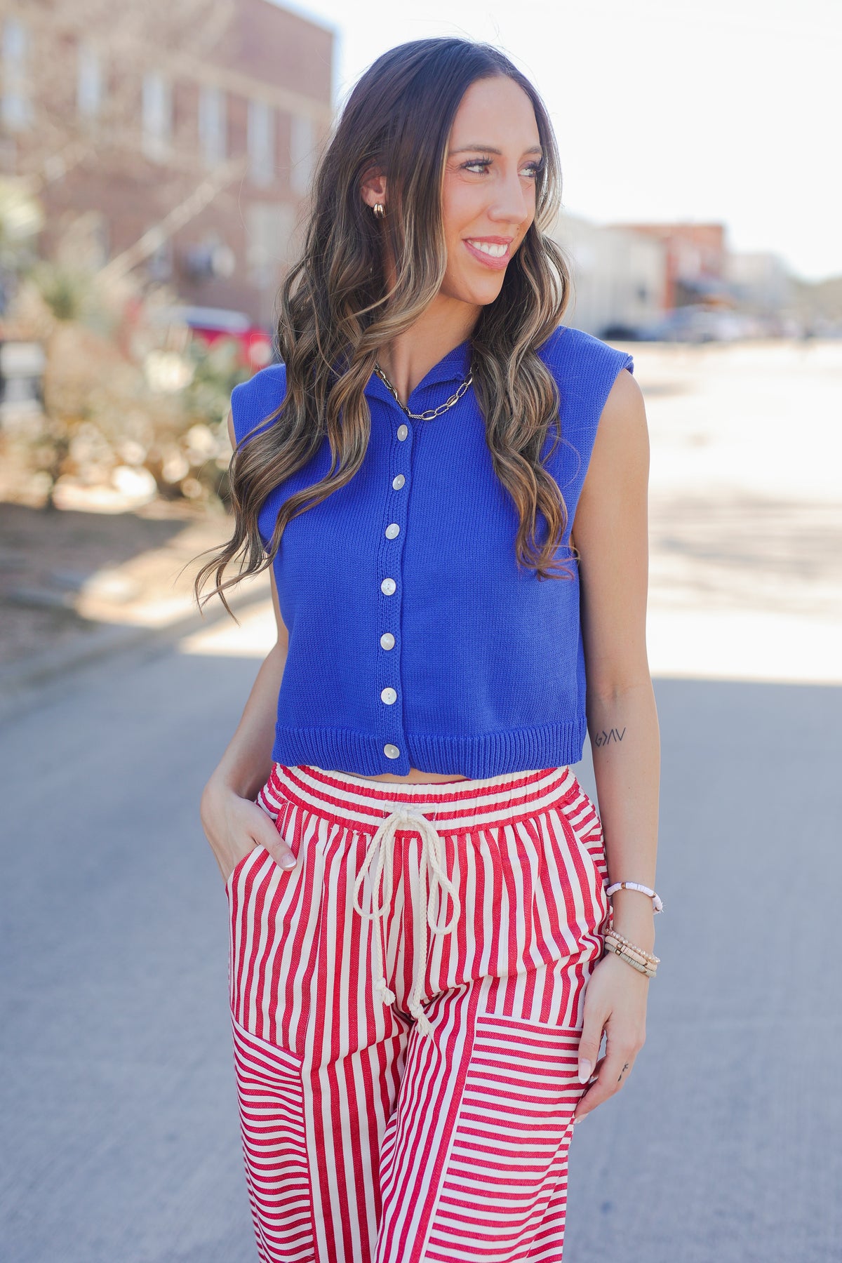 Woman wearing a blue sleeveless cardigan and red and white striped pants on a street.