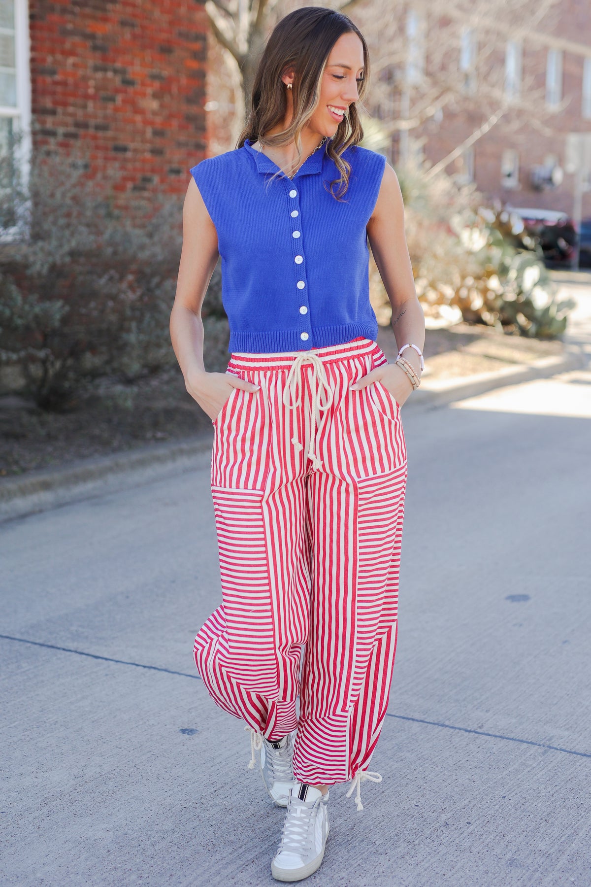Woman wearing a blue sleeveless top and red and white striped pants on a street.